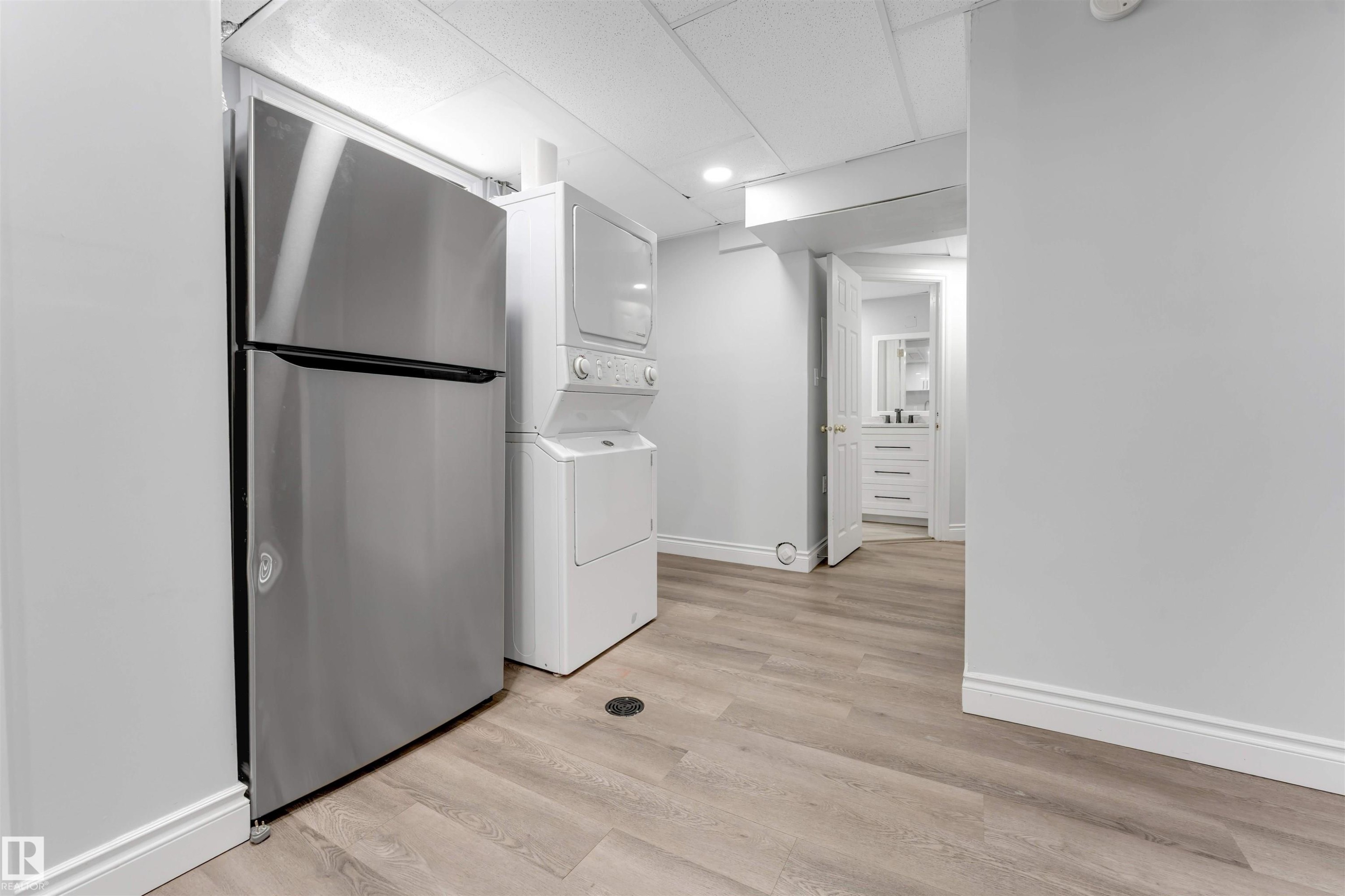Stainless steel refrigerator, stacked laundry appliances, and light wood-finish flooring - 7419 33 Avenue Nw, Edmonton, AB - Indoor Photo Showing Laundry Room