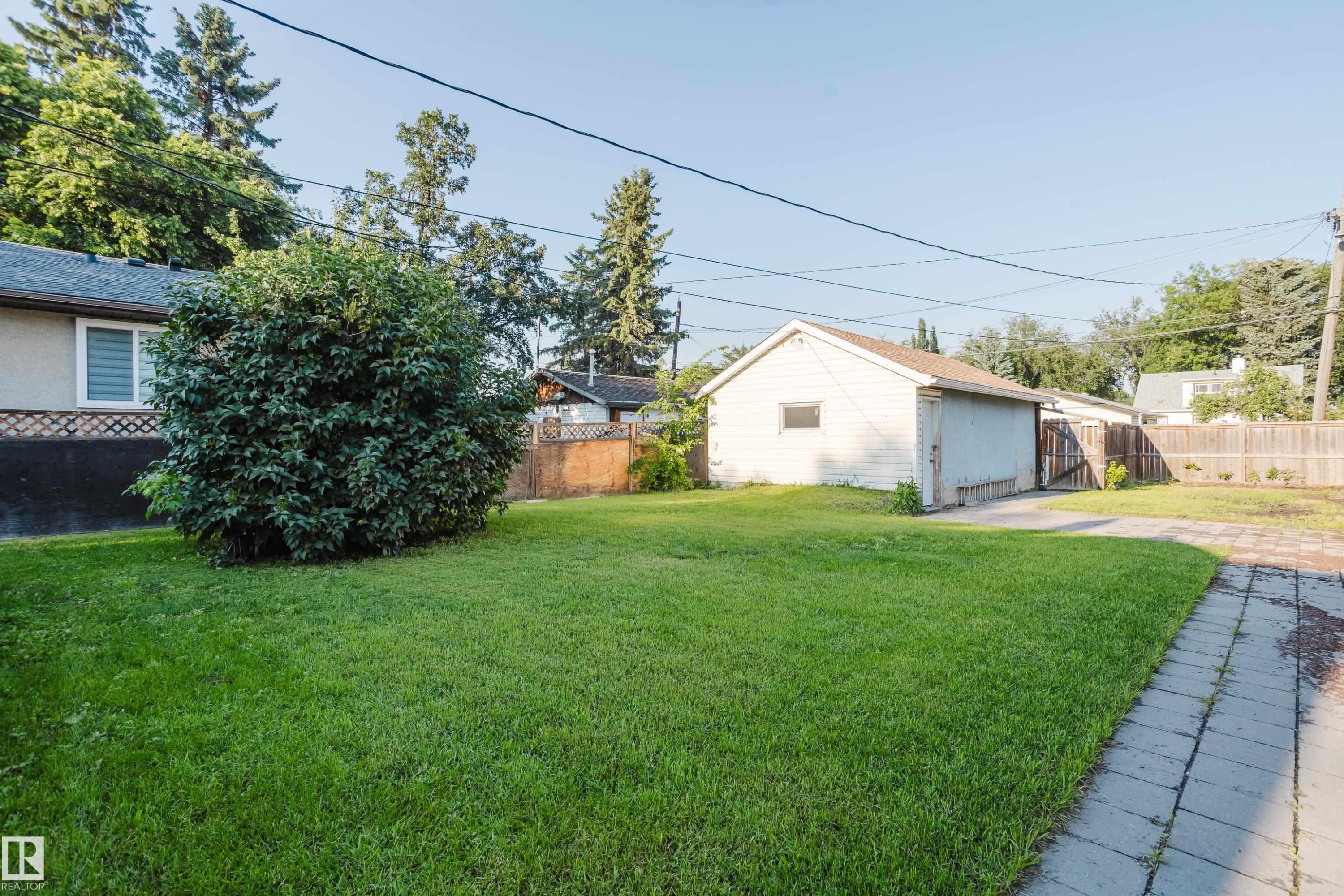 Spacious backyard featuring a large lawn, mature shrubbery, a detached garage, and a paved walkway - 12431 81 Street Nw, Edmonton, AB - Outdoor