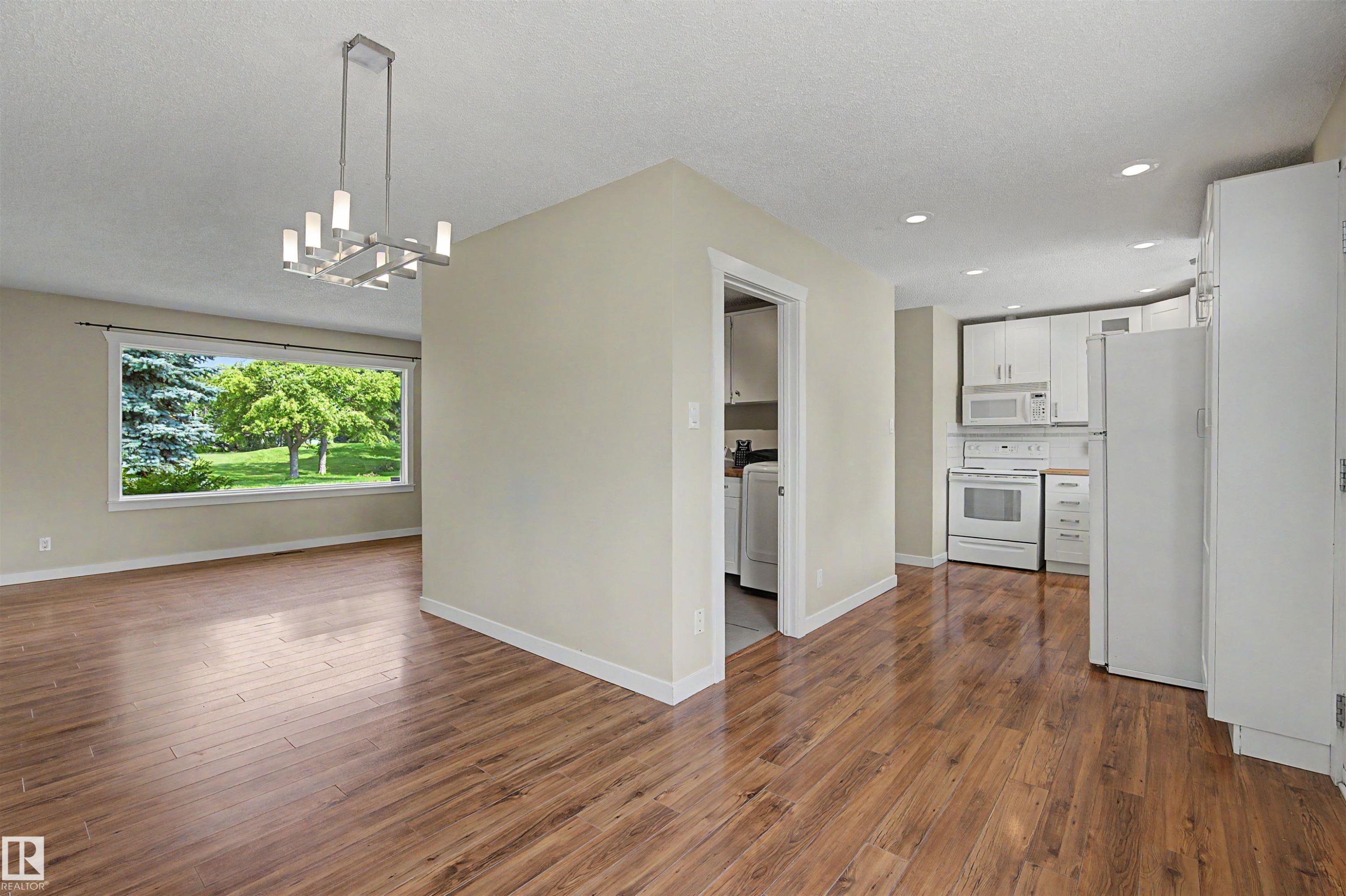 Open-concept living space featuring wood-finish flooring, a contemporary chandelier, and a large picture window - 8823 130A Avenue Nw, Edmonton, AB - Indoor
