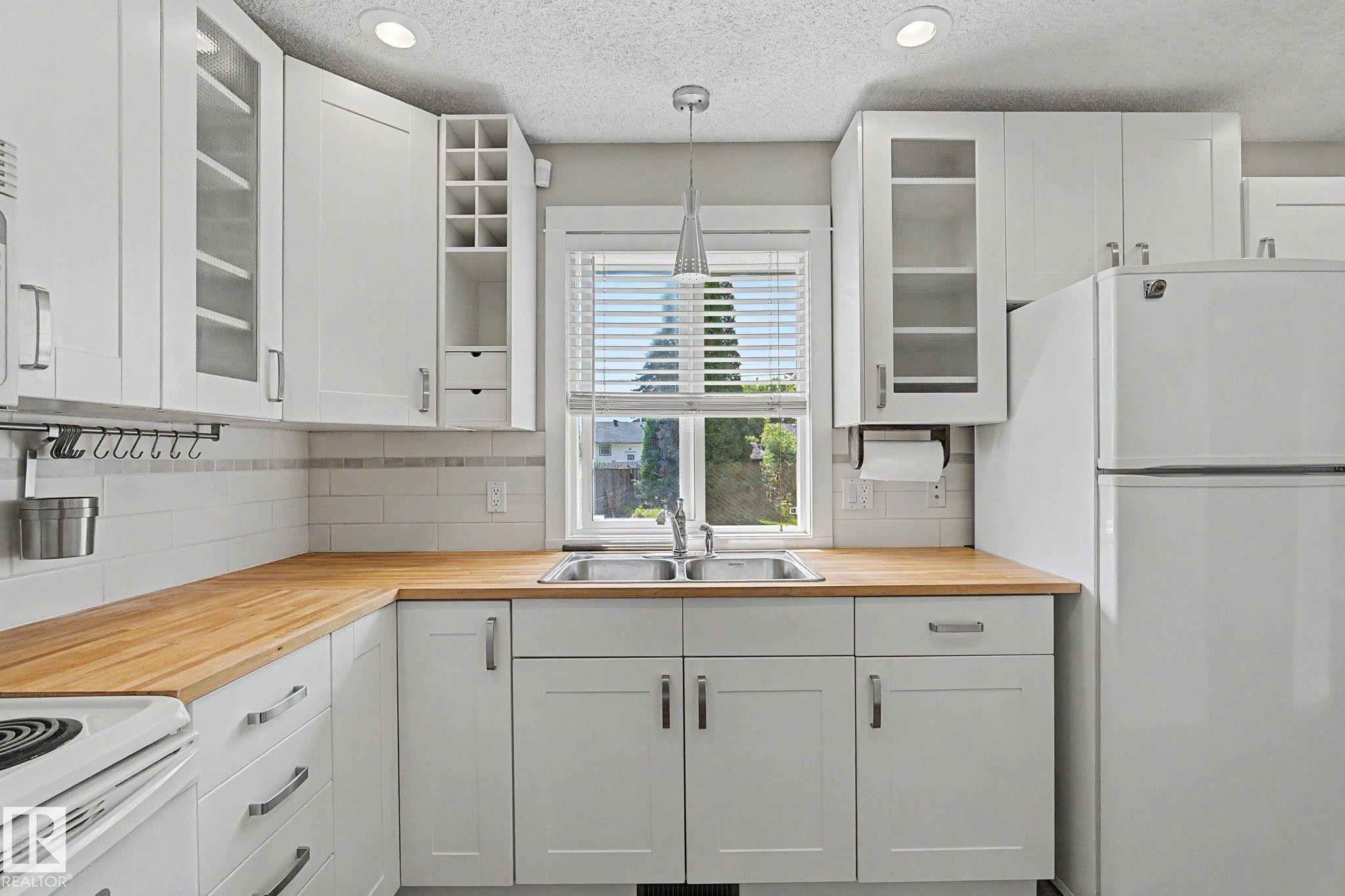 Kitchen featuring abundant white cabinetry, butcher block countertops, stainless steel sink, and recessed lighting - 8823 130A Avenue Nw, Edmonton, AB - Indoor Photo Showing Kitchen With Double Sink