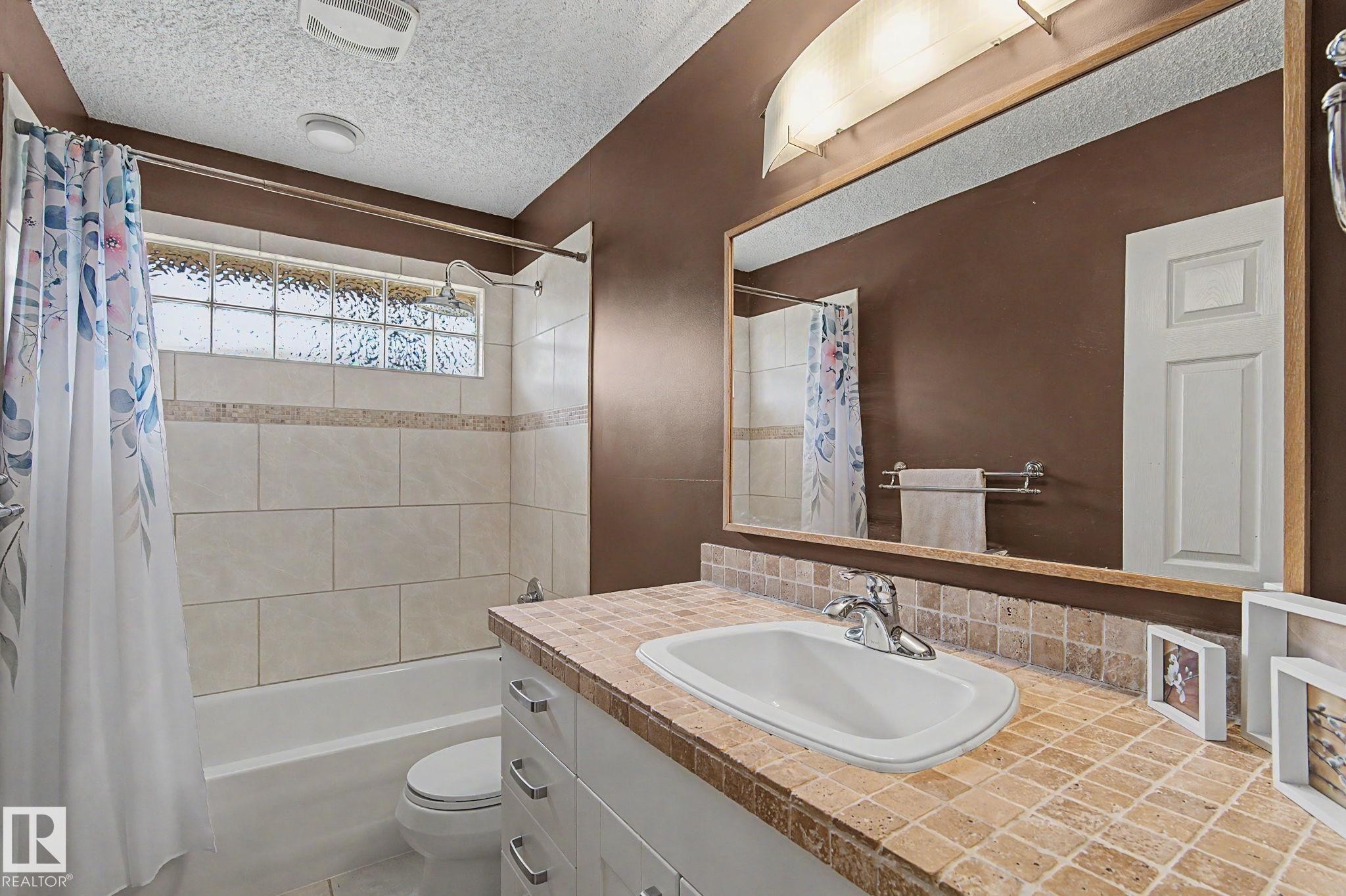Bathroom featuring a white vanity with a tiled countertop, a built-in sink, and a large mirror - 8823 130A Avenue Nw, Edmonton, AB - Indoor Photo Showing Bathroom