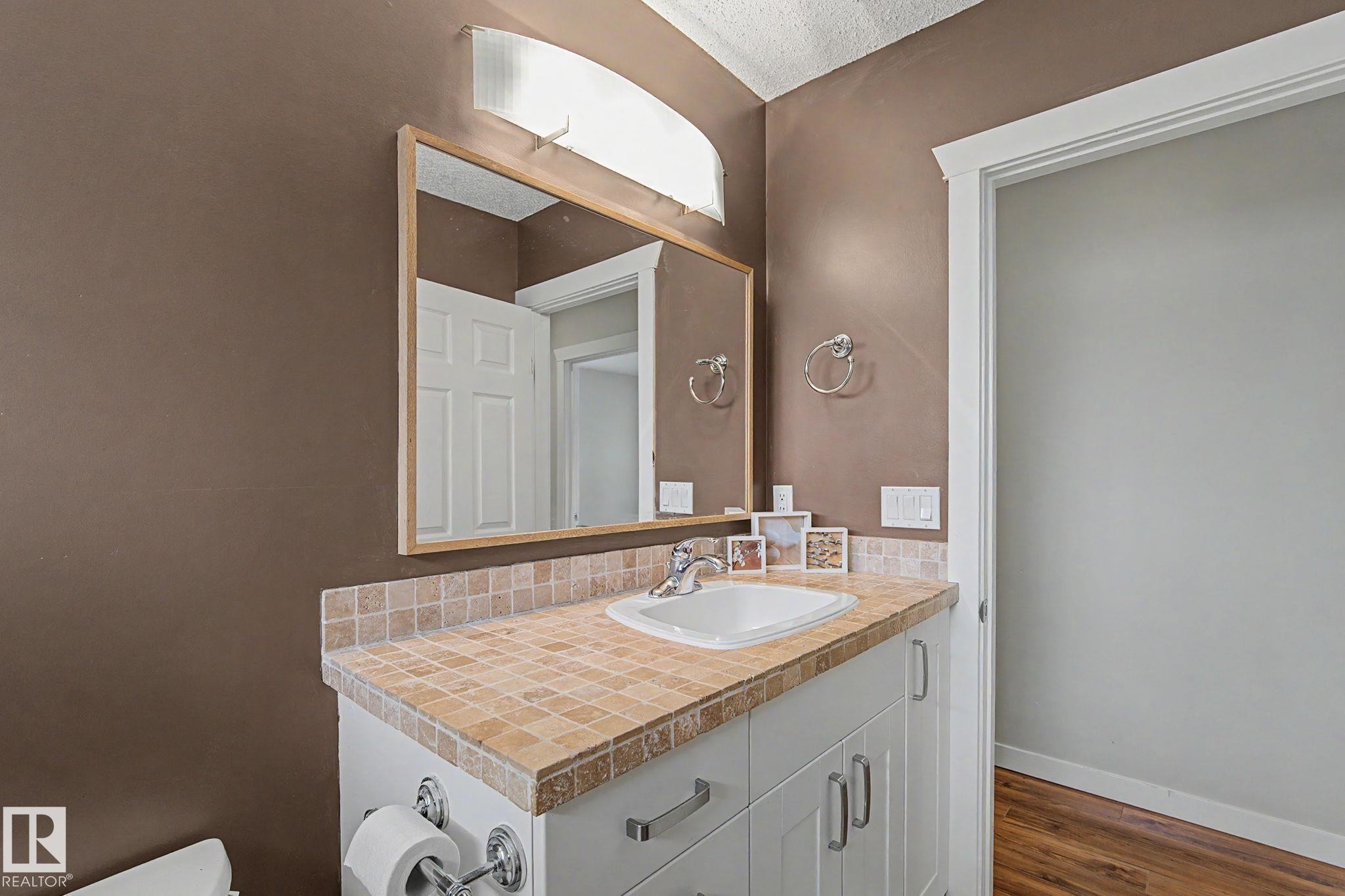 Bathroom vanity with a neutral tile countertop, integrated sink, and white cabinetry - 8823 130A Avenue Nw, Edmonton, AB - Indoor Photo Showing Bathroom