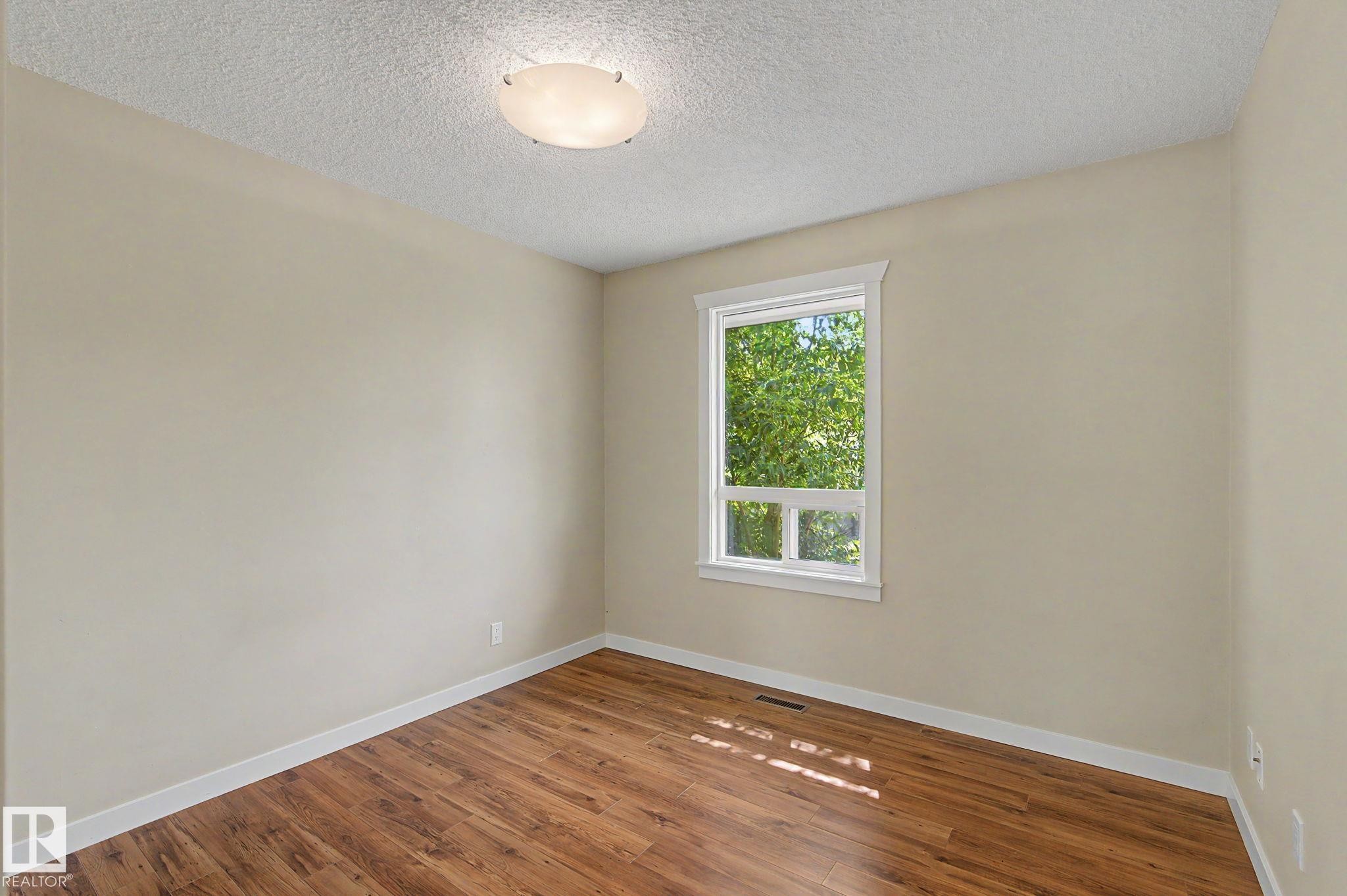 Bright interior space featuring wood-finish flooring, neutral-toned walls, and a white-trimmed window - 8823 130A Avenue Nw, Edmonton, AB - Indoor Photo Showing Other Room