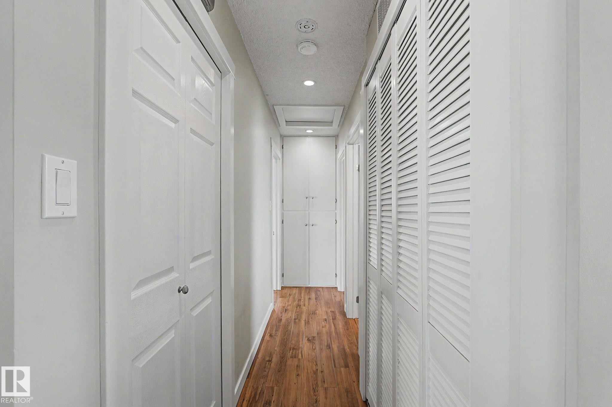 Hallway featuring wood-finish flooring, recessed lighting, white panel doors, louvered closet doors, and white walls - 8823 130A Avenue Nw, Edmonton, AB - Indoor Photo Showing Other Room