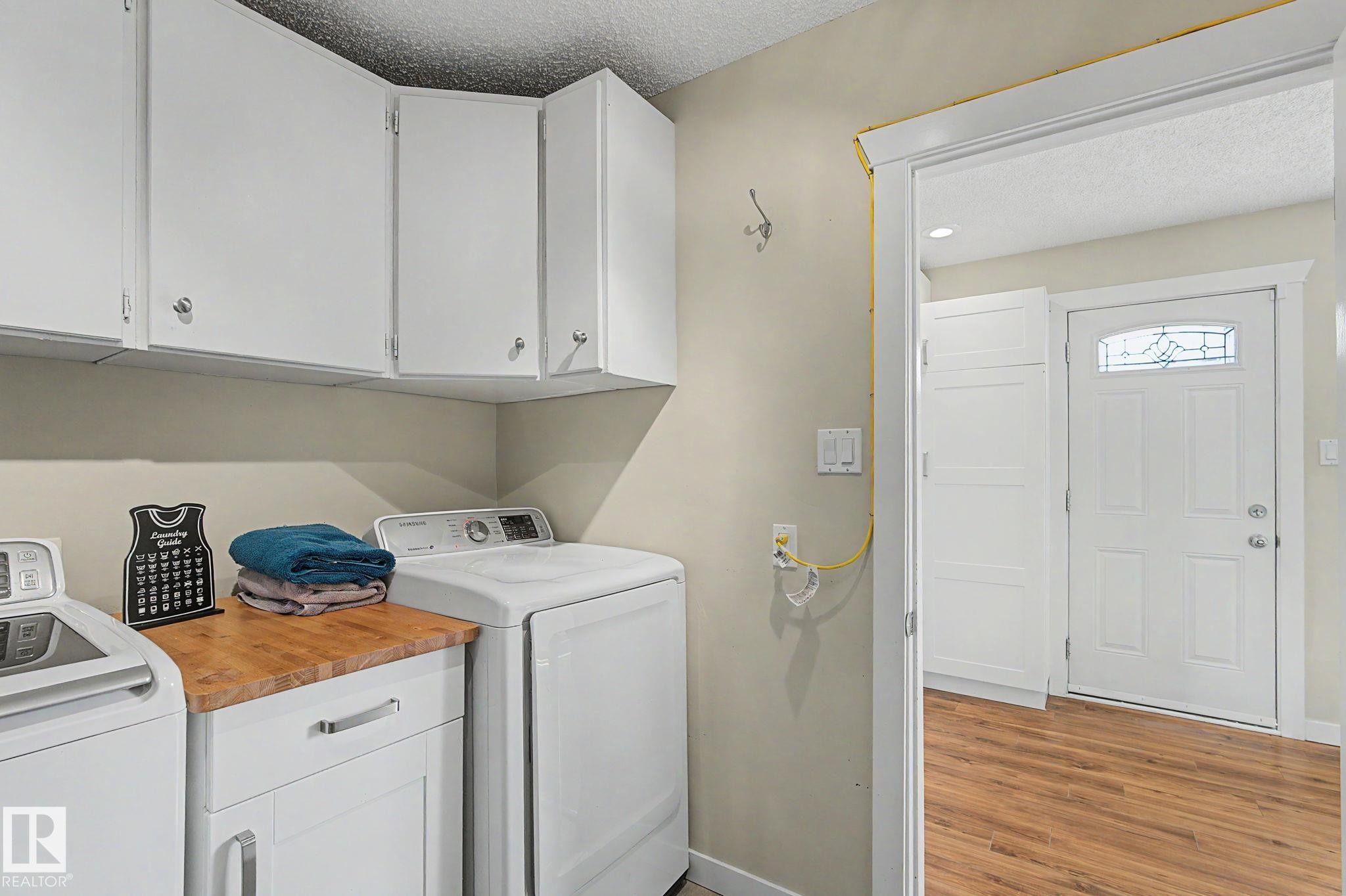 Dedicated laundry space featuring white cabinetry, a wood-finish countertop, and ample overhead storage - 8823 130A Avenue Nw, Edmonton, AB - Indoor Photo Showing Laundry Room