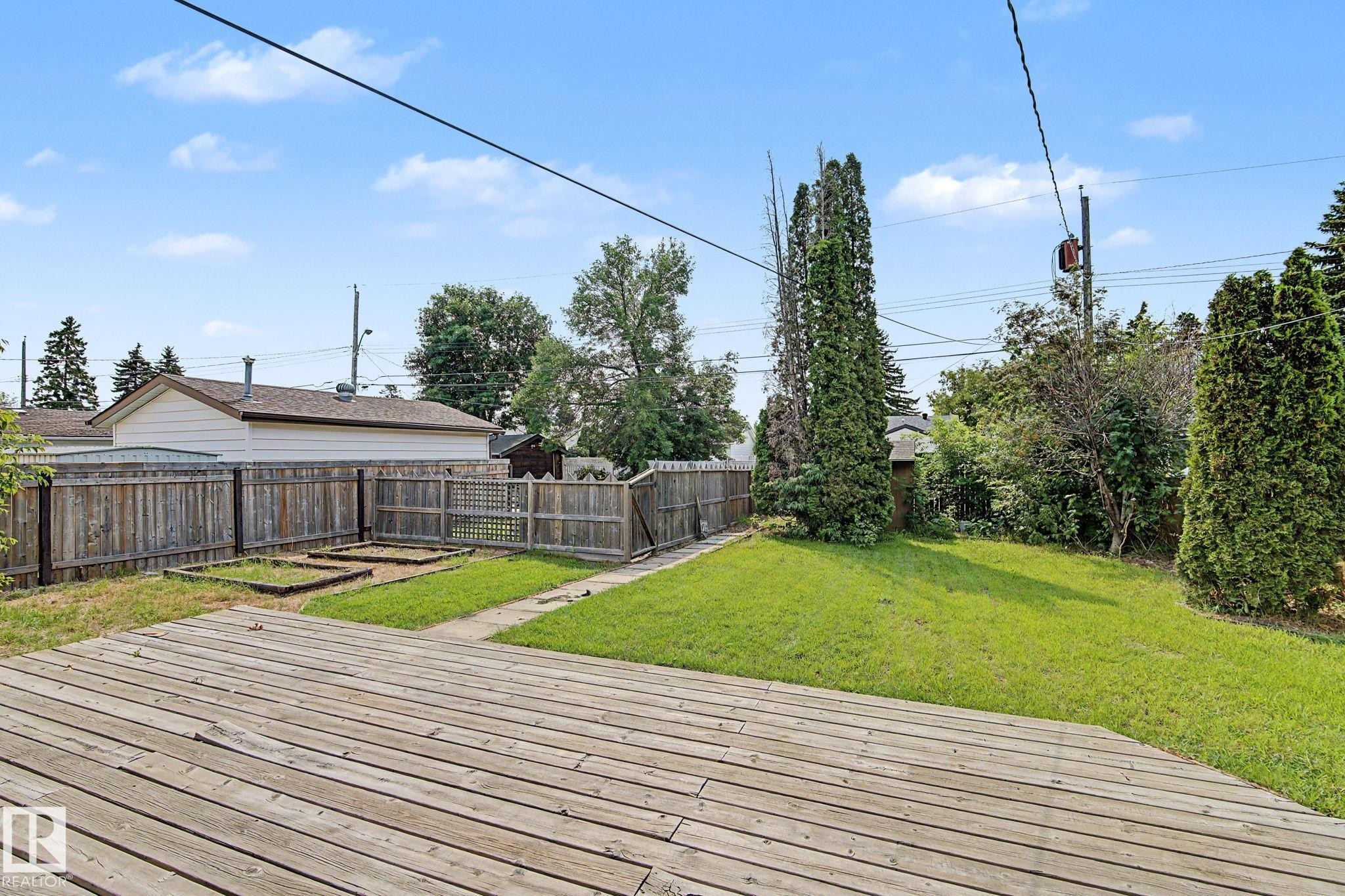 Expansive backyard featuring a spacious wood deck, manicured lawn, raised garden beds, and mature perimeter trees - 8823 130A Avenue Nw, Edmonton, AB - Outdoor