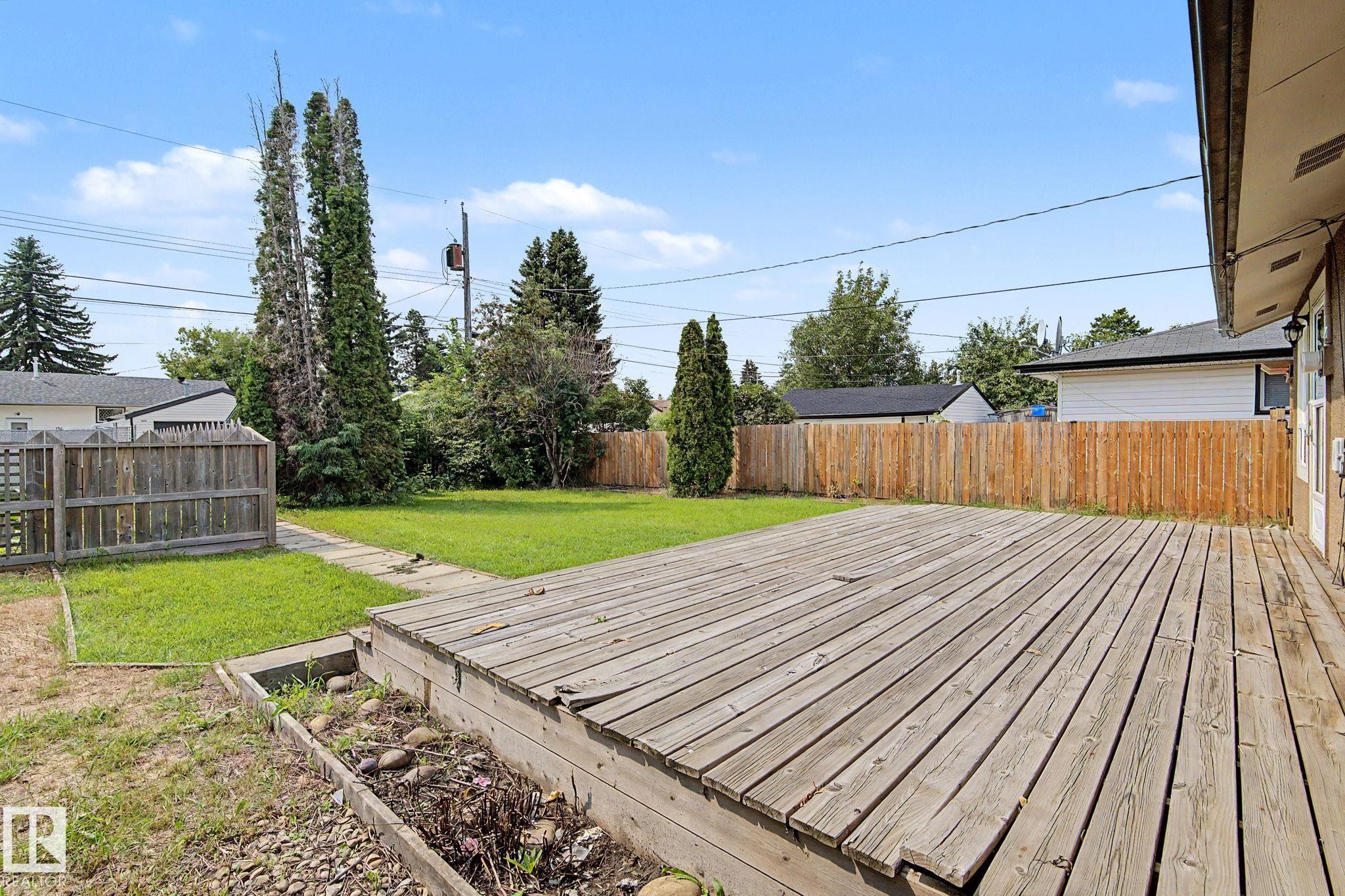 Expansive backyard featuring a large wooden deck, manicured lawn, and privacy fencing - 8823 130A Avenue Nw, Edmonton, AB - Outdoor
