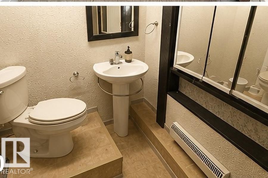 Pedestal sink with chrome faucet, framed mirror, and toilet with a white seat - 7812 144 Avenue Nw, Edmonton, AB - Indoor Photo Showing Bathroom
