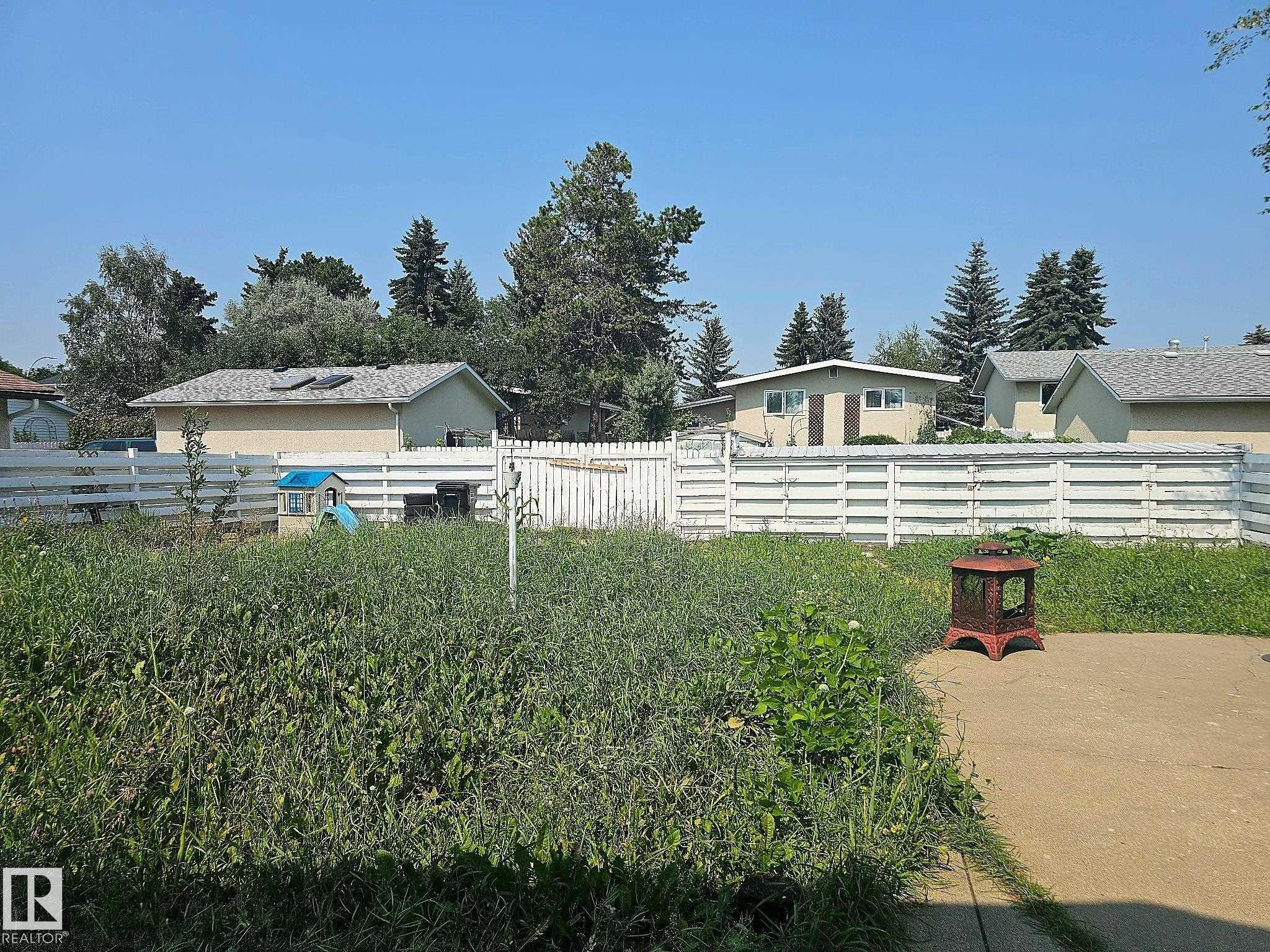 Fenced backyard with a concrete patio area and mature perimeter trees - 7812 144 Avenue Nw, Edmonton, AB - Outdoor