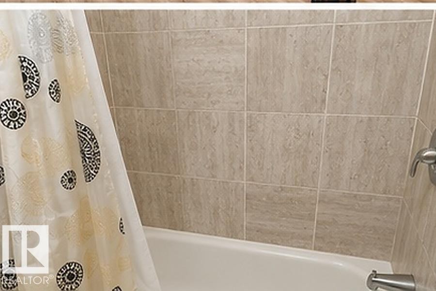 Bathtub with light-toned tiled surround and brushed nickel fixtures - 7812 144 Avenue Nw, Edmonton, AB - Indoor Photo Showing Bathroom