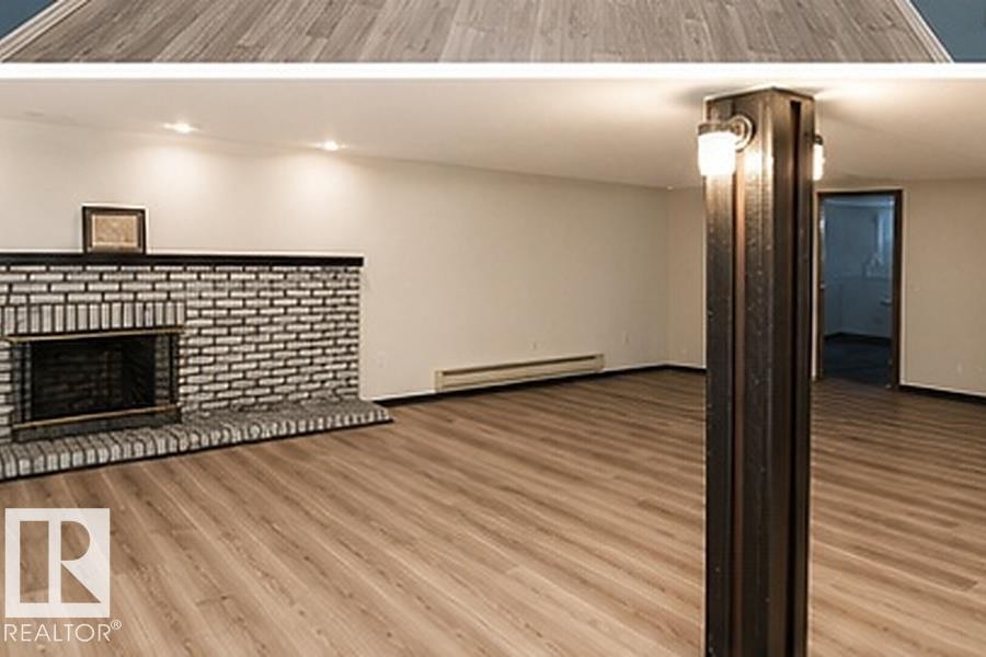 Spacious room with wood-finish flooring, a brick fireplace with a black mantel, recessed lighting, and wall-mounted sconces on a structural column - 7812 144 Avenue Nw, Edmonton, AB - Indoor With Fireplace