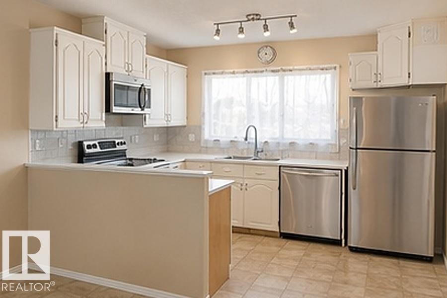Kitchen featuring white cabinetry, stainless steel appliances, a white tile backsplash, a window above the sink, and track lighting - 7812 144 Avenue Nw, Edmonton, AB - Indoor Photo Showing Kitchen