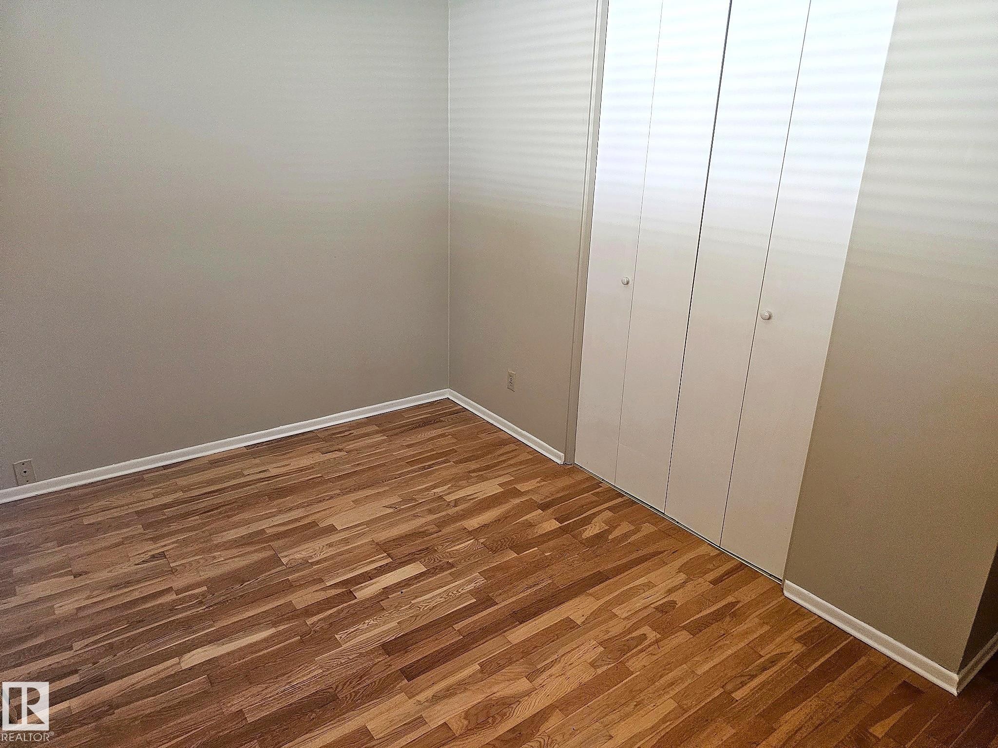 Room featuring wood-finish flooring, light neutral wall paint, white baseboards, and a white bi-fold closet - 7812 144 Avenue Nw, Edmonton, AB - Indoor Photo Showing Other Room