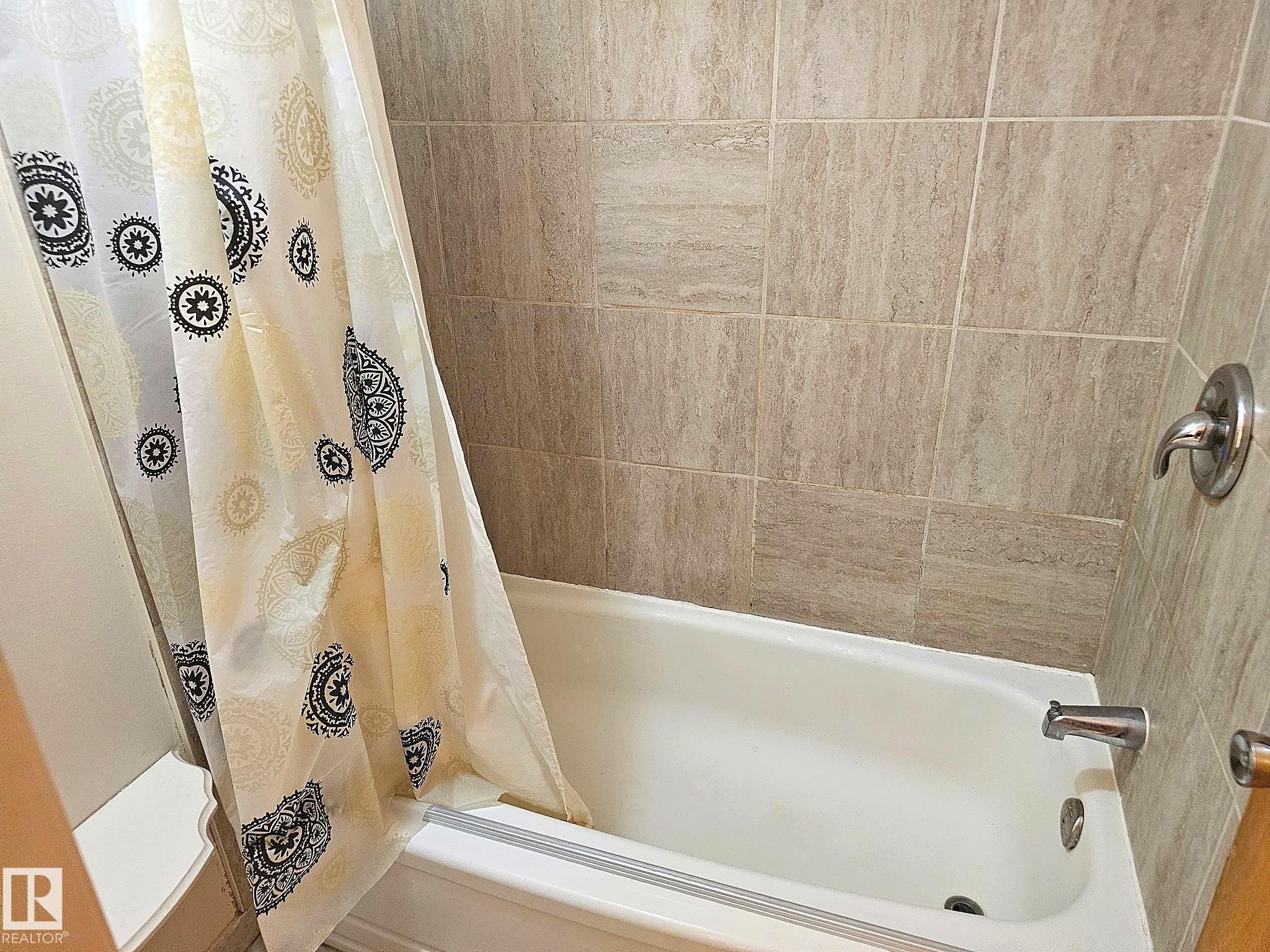 Bathtub with beige tile surround featuring a chrome showerhead and faucet - 7812 144 Avenue Nw, Edmonton, AB - Indoor Photo Showing Bathroom