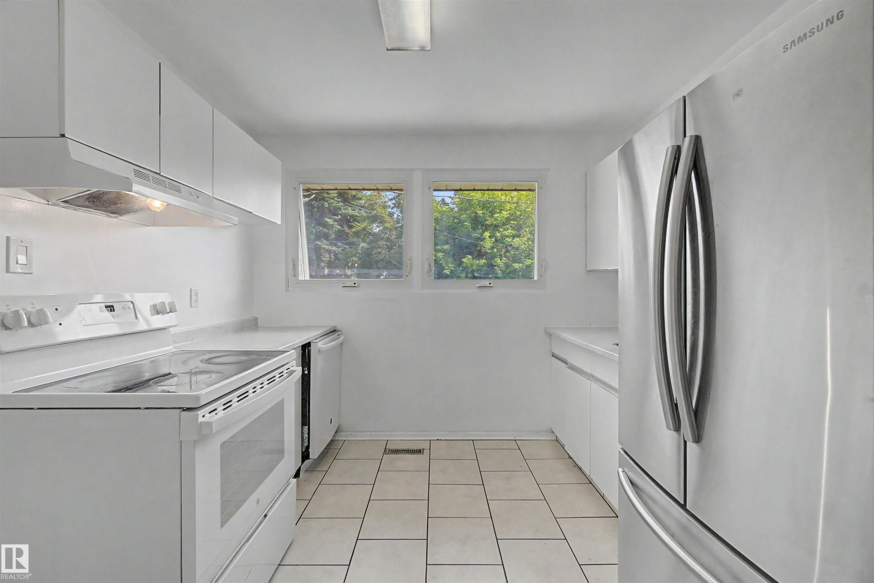 Kitchen featuring white cabinetry, white solid surface countertops, white tile flooring, white electric range, and a stainless steel refrigerator - 8215 149 Street Nw, Edmonton, AB - Indoor Photo Showing Laundry Room