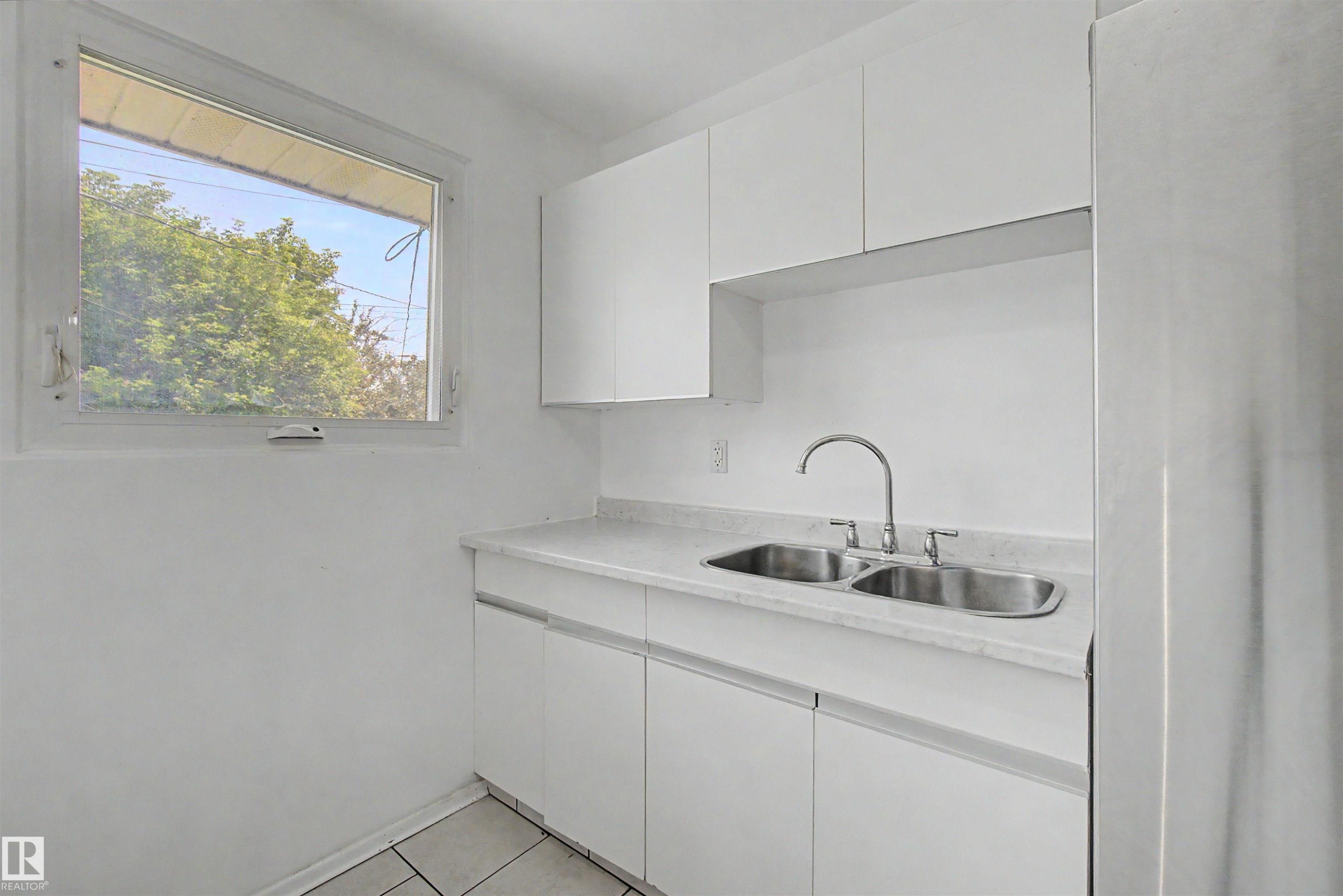 Kitchen featuring white cabinetry, light-colored countertops, a double basin stainless steel sink with a gooseneck faucet, and a window - 8215 149 Street Nw, Edmonton, AB - Indoor Photo Showing Kitchen With Double Sink