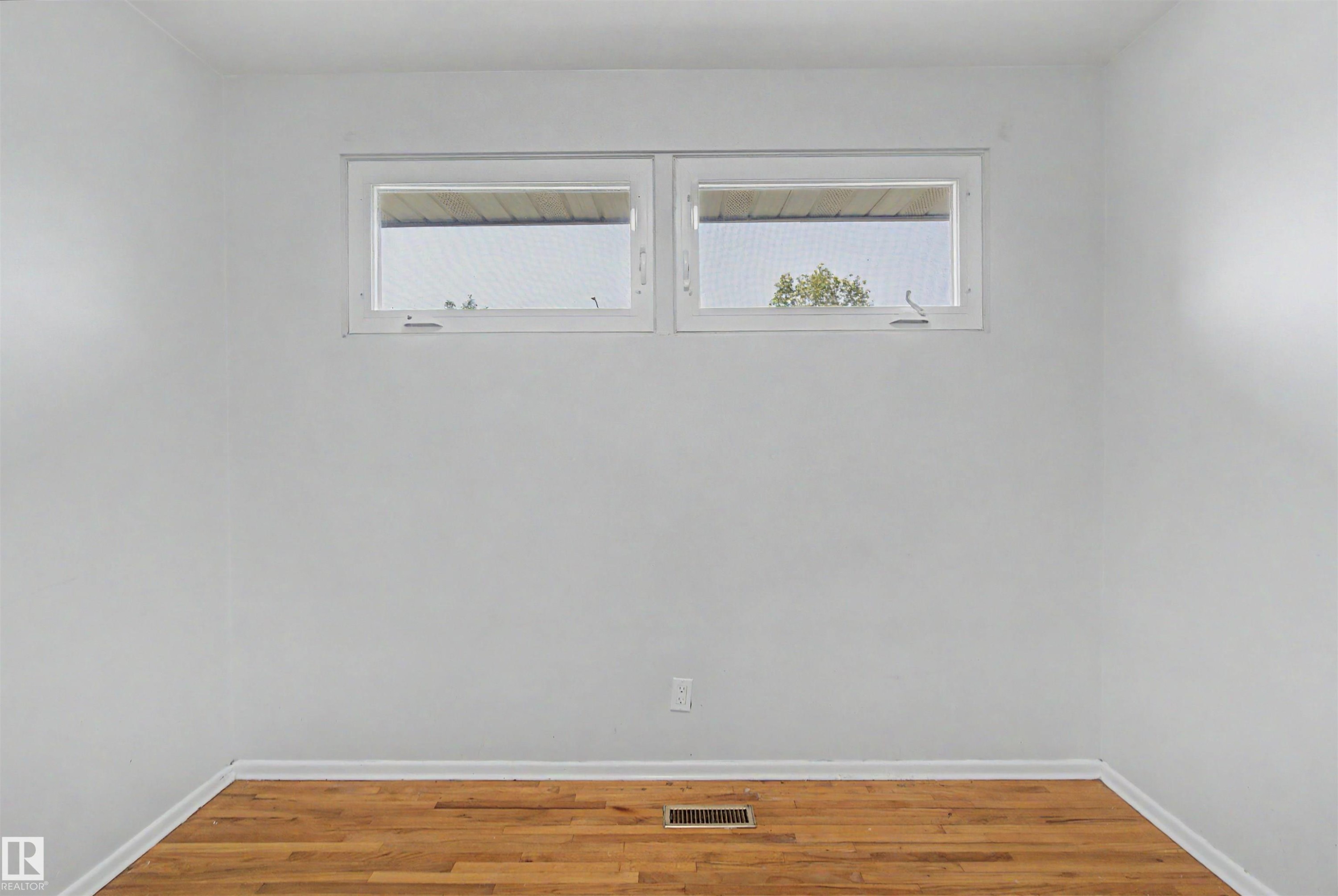 Bright room featuring wood-finish flooring, white painted walls, and two horizontal windows - 8215 149 Street Nw, Edmonton, AB - Indoor Photo Showing Other Room