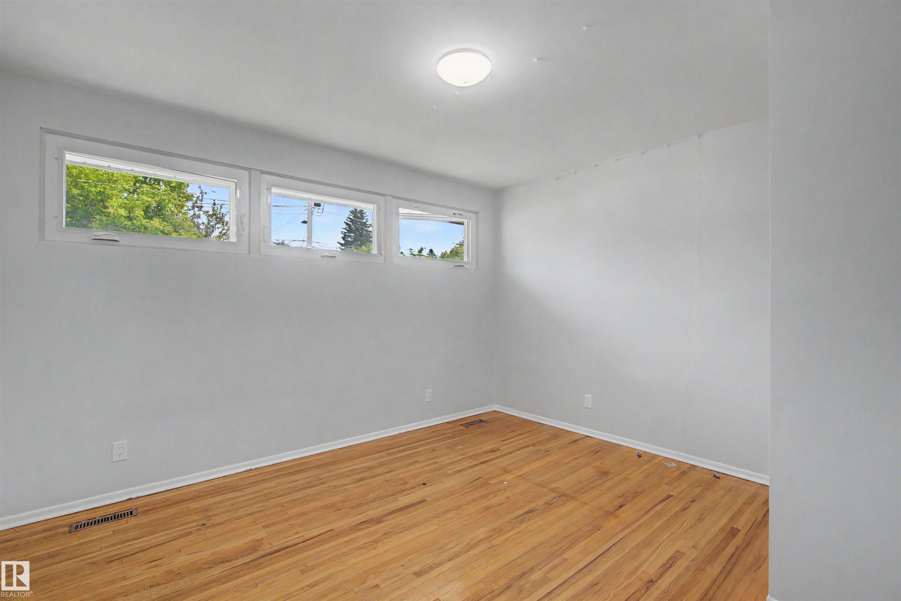 Room featuring three horizontal transom windows, wood-finish flooring, white baseboards, and a flush-mount ceiling light fixture - 8215 149 Street Nw, Edmonton, AB - Indoor Photo Showing Other Room