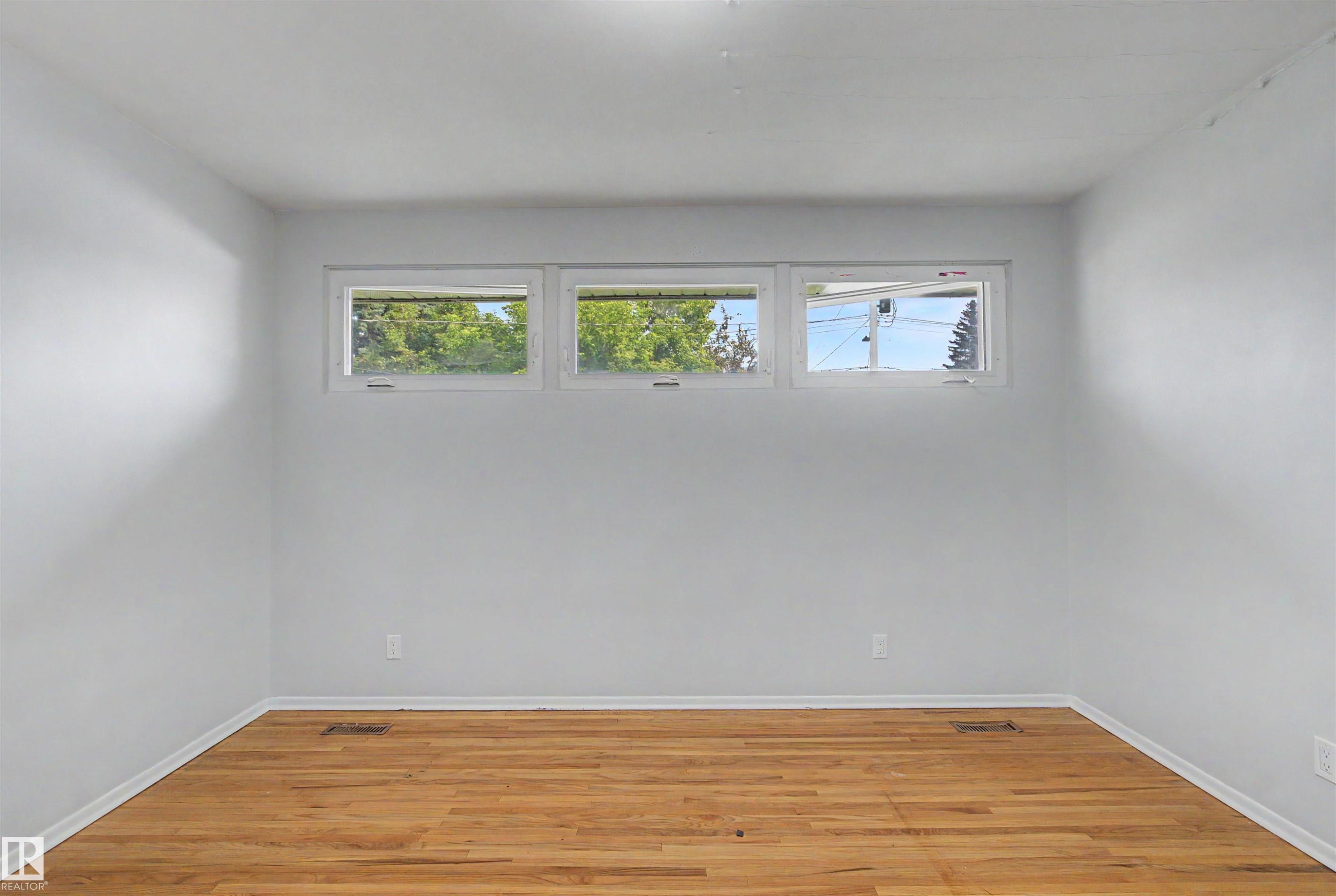 Hardwood flooring throughout a room featuring light-colored walls and a trio of horizontal windows - 8215 149 Street Nw, Edmonton, AB - Indoor Photo Showing Other Room