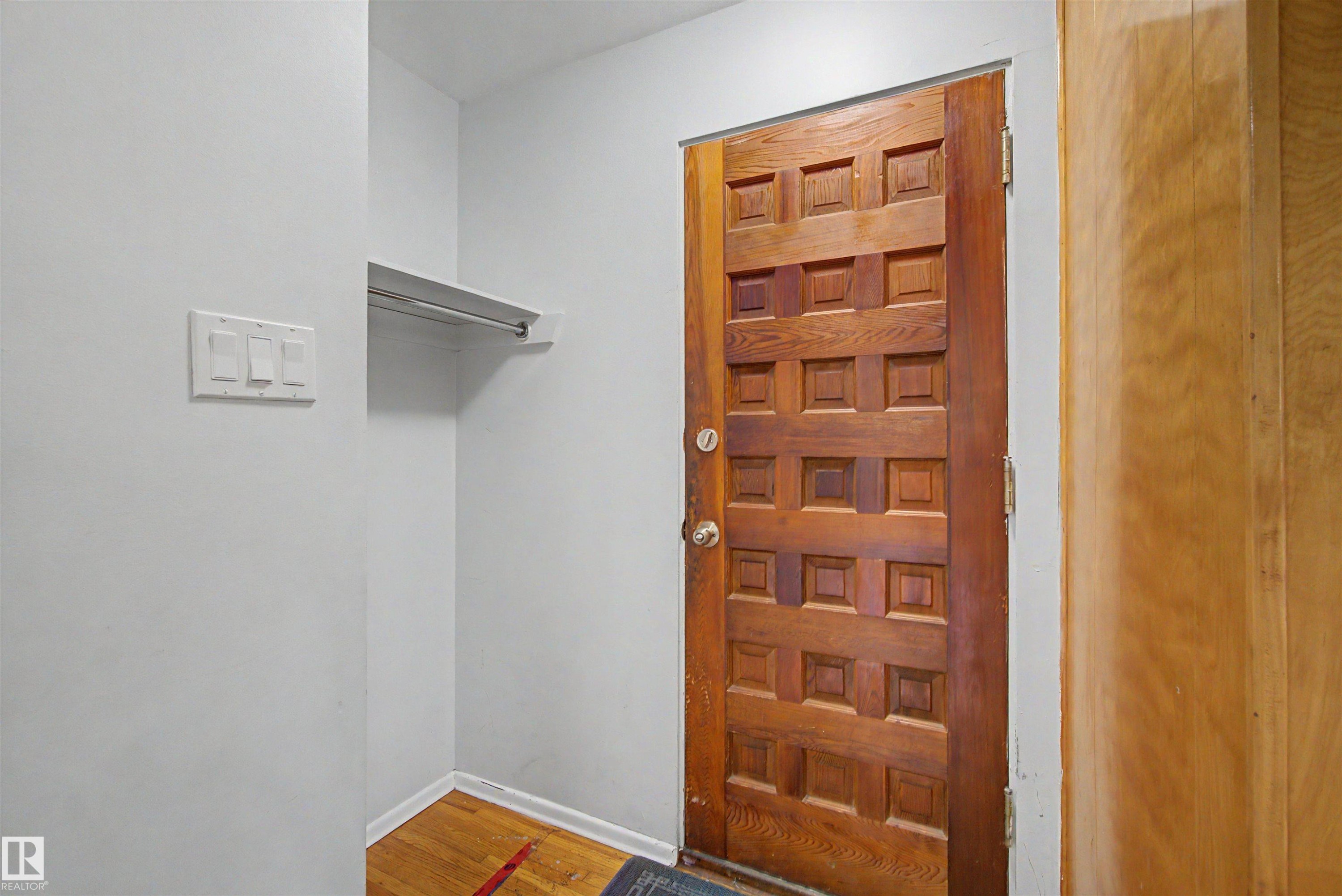 Solid wood entry door with square panel design, wood-finish flooring, and integrated coat closet with shelf and hanging rod - 8215 149 Street Nw, Edmonton, AB - Indoor