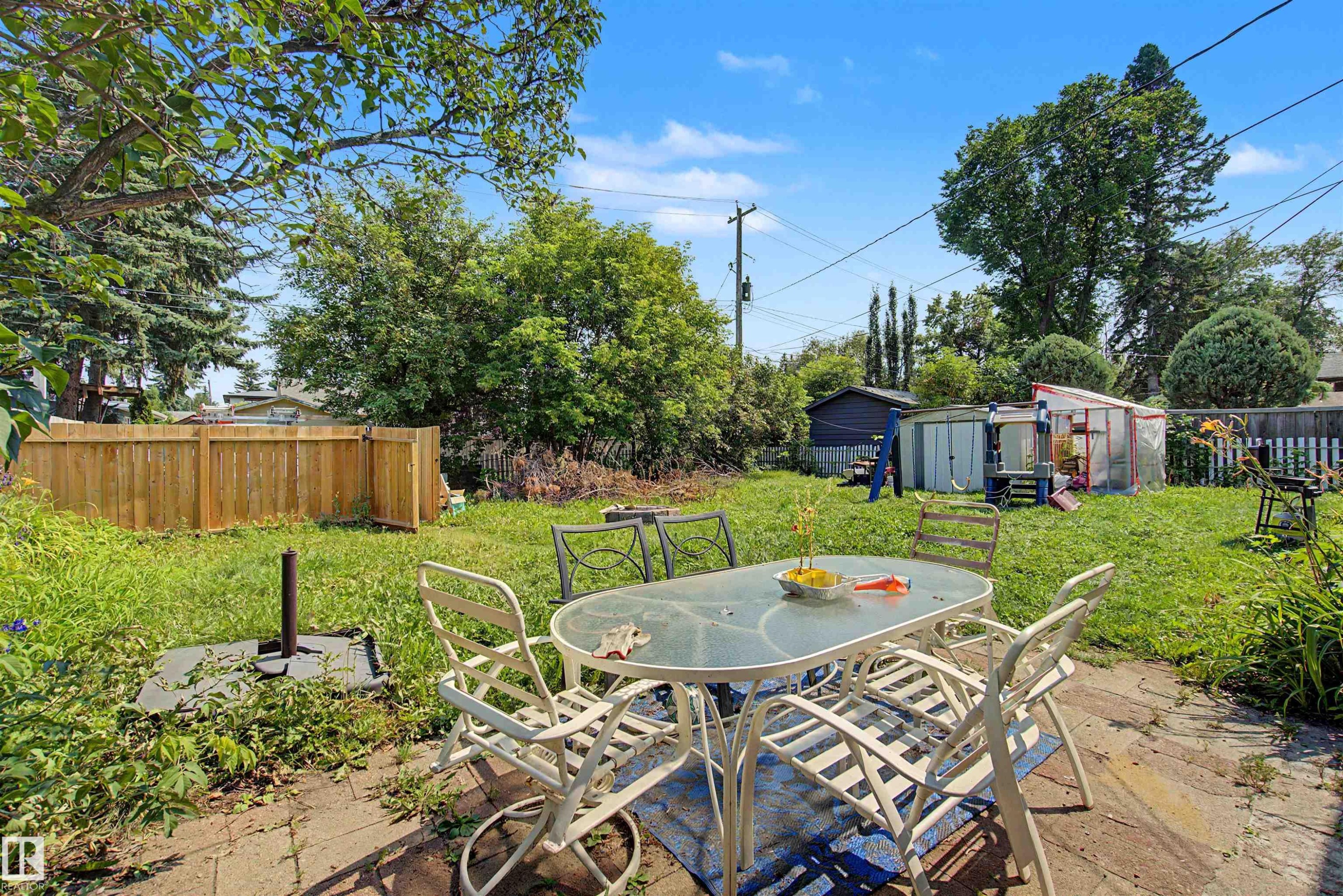 Expansive backyard featuring a patio area with paver stones, a wood privacy fence, and a diverse assortment of mature trees and shrubbery - 8215 149 Street Nw, Edmonton, AB - Outdoor With Backyard