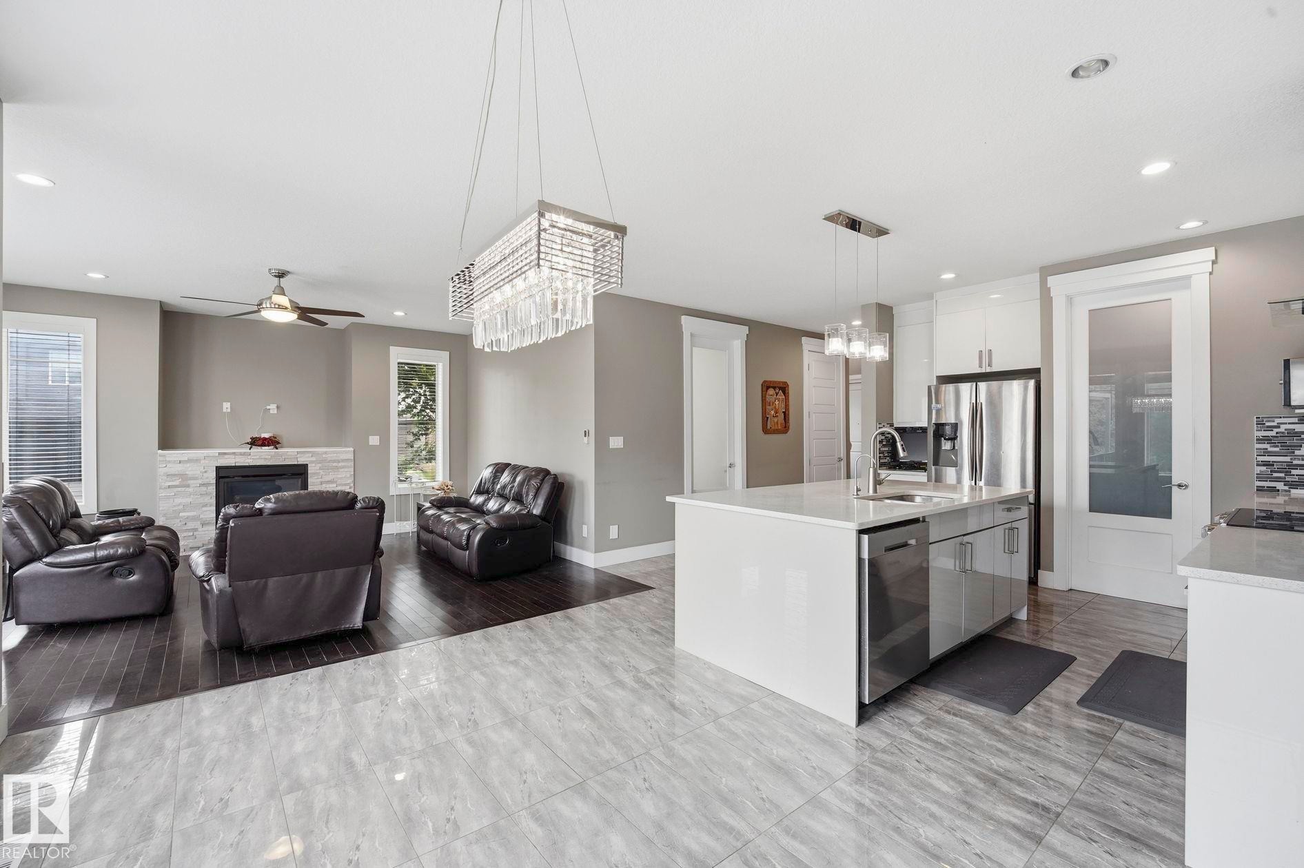 Open-concept living space featuring a central kitchen island with a built-in sink and stainless steel appliances - 1051 174 Street Sw, Edmonton, AB - Indoor