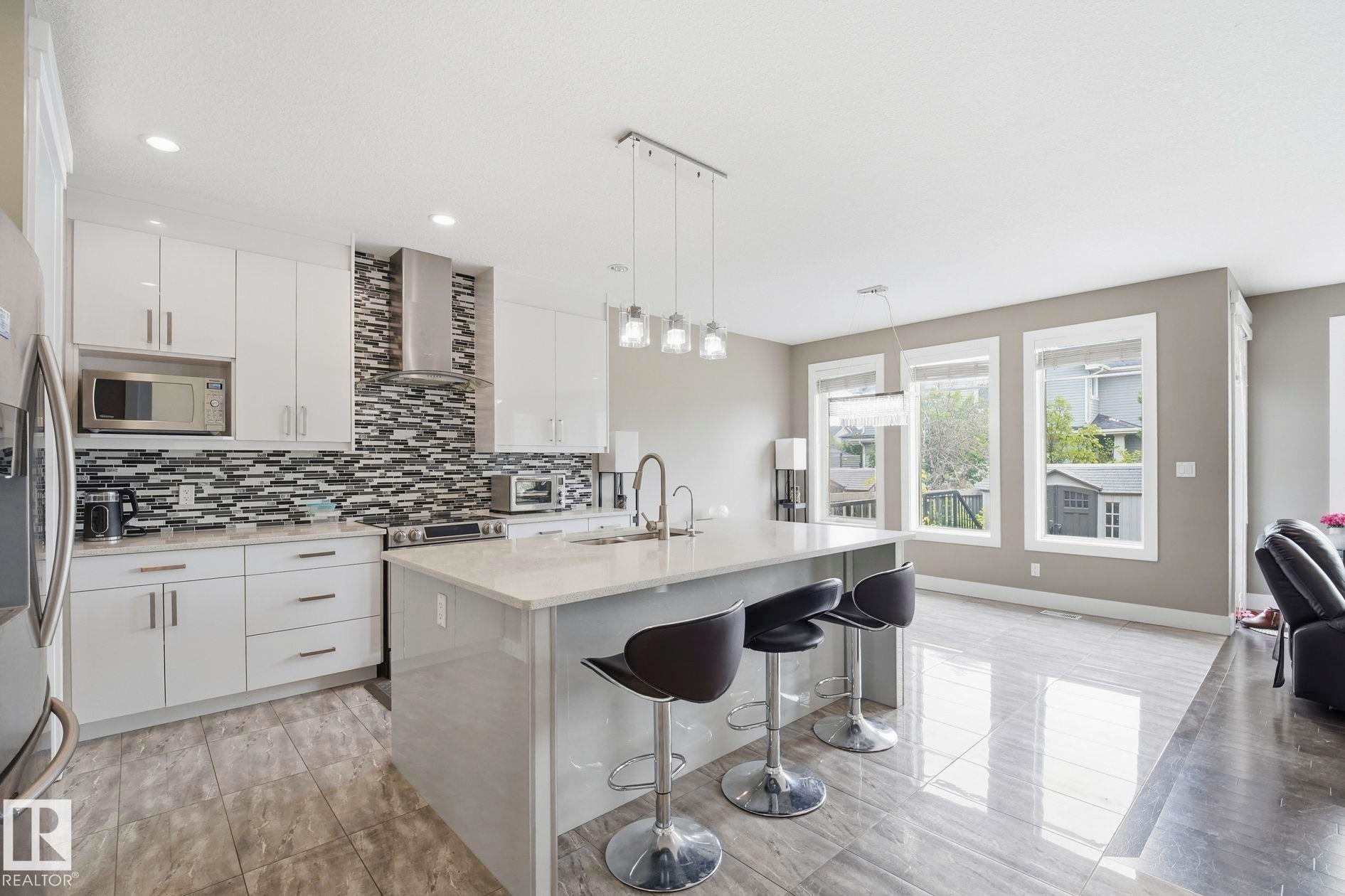 Contemporary kitchen featuring a large center island with seating, white shaker cabinetry, stainless steel appliances, and a mosaic tile backsplash - 1051 174 Street Sw, Edmonton, AB - Indoor Photo Showing Kitchen With Upgraded Kitchen