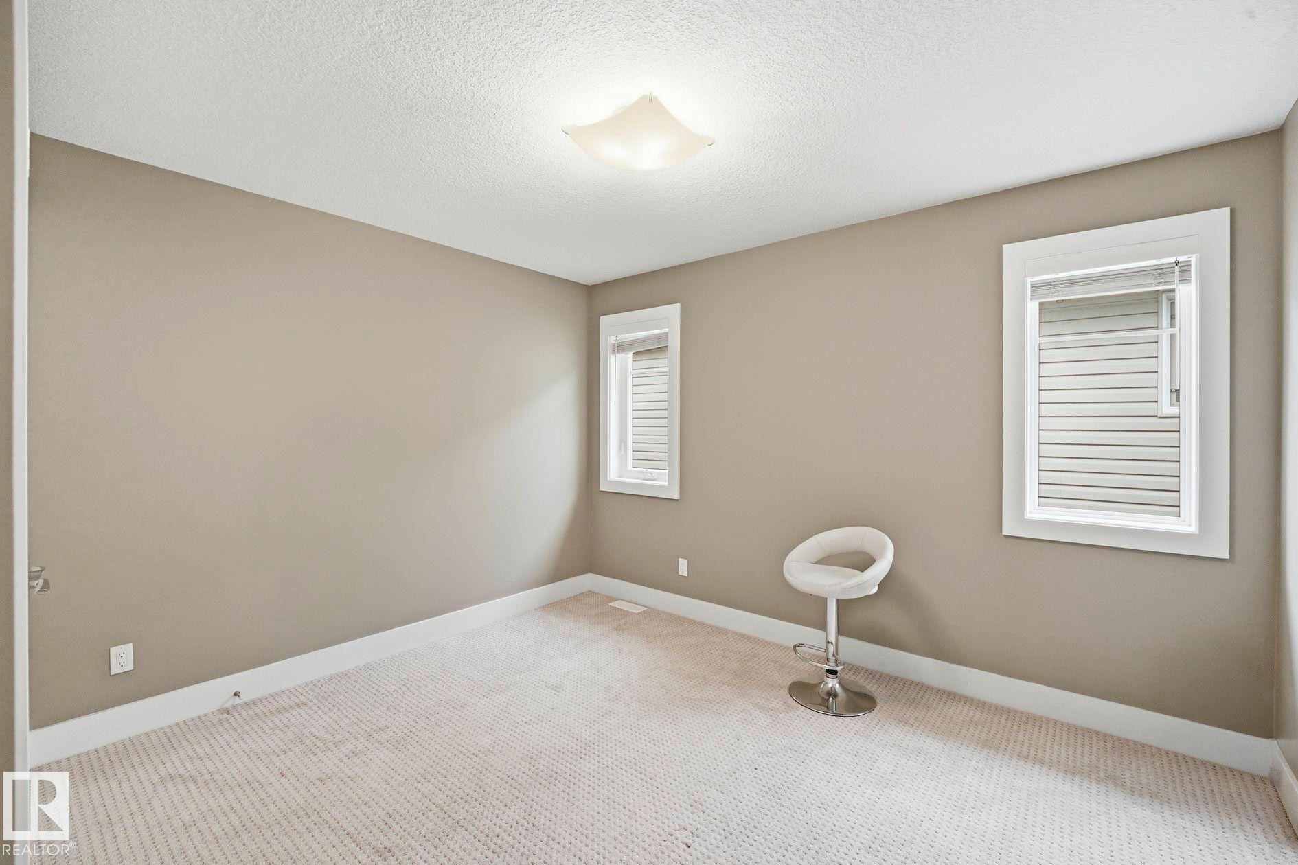 Carpeted room featuring two windows with blinds, a neutral wall color, white trim, and a ceiling-mounted light fixture - 1051 174 Street Sw, Edmonton, AB - Indoor Photo Showing Other Room