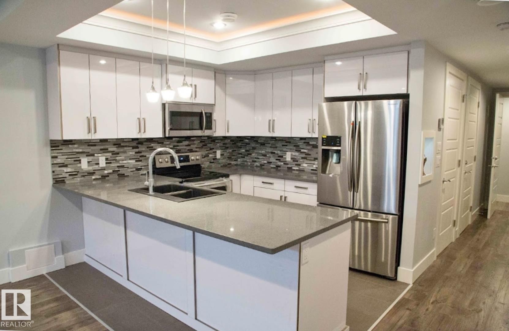 Contemporary kitchen featuring white cabinetry, stainless steel appliances, a mosaic tile backsplash, and an island with a double sink - 1051 174 Street Sw, Edmonton, AB - Indoor Photo Showing Kitchen With Double Sink With Upgraded Kitchen