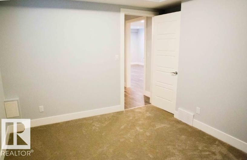 Neutral gray walls with white trim, tan carpeting, and a modern white door with horizontal paneling - 1051 174 Street Sw, Edmonton, AB - Indoor Photo Showing Other Room
