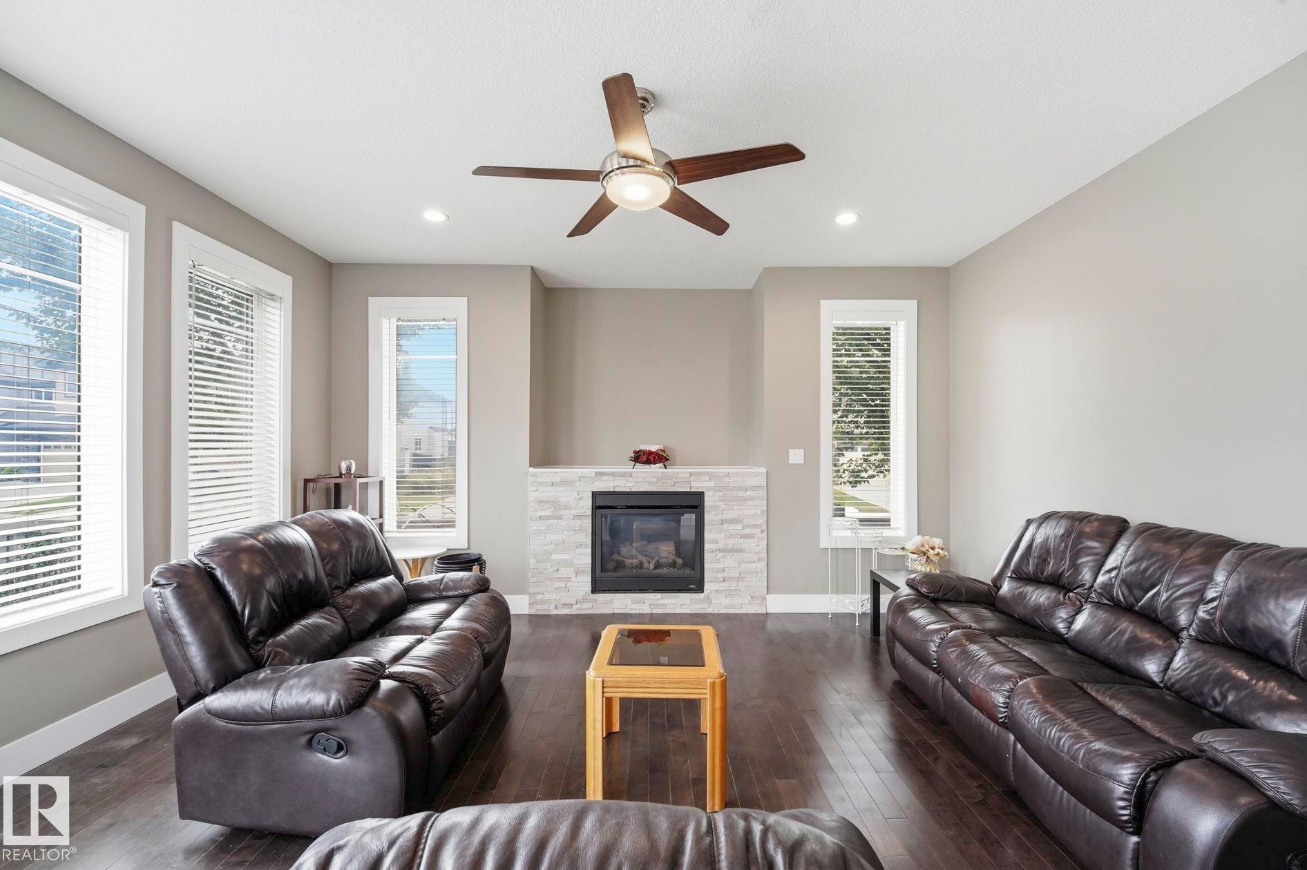 Living area featuring dark wood-finish flooring, light grey walls, and a recessed ceiling with a contemporary ceiling fan - 1051 174 Street Sw, Edmonton, AB - Indoor Photo Showing Living Room With Fireplace
