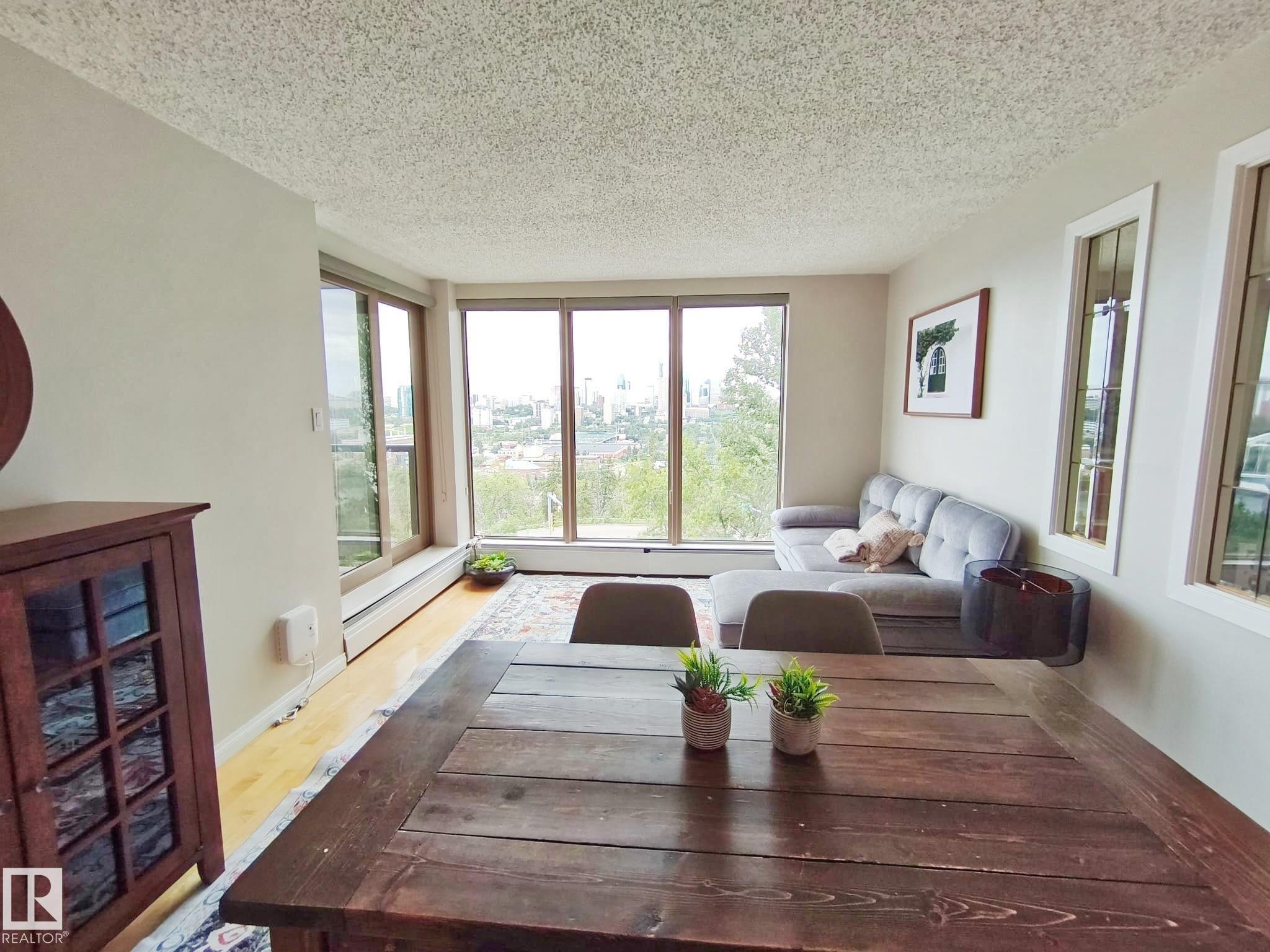 Open-concept living space featuring expansive windows, wood-finish flooring, and light-toned walls - #509 10149 Saskatchewan Dr Nw, Edmonton, AB - Indoor
