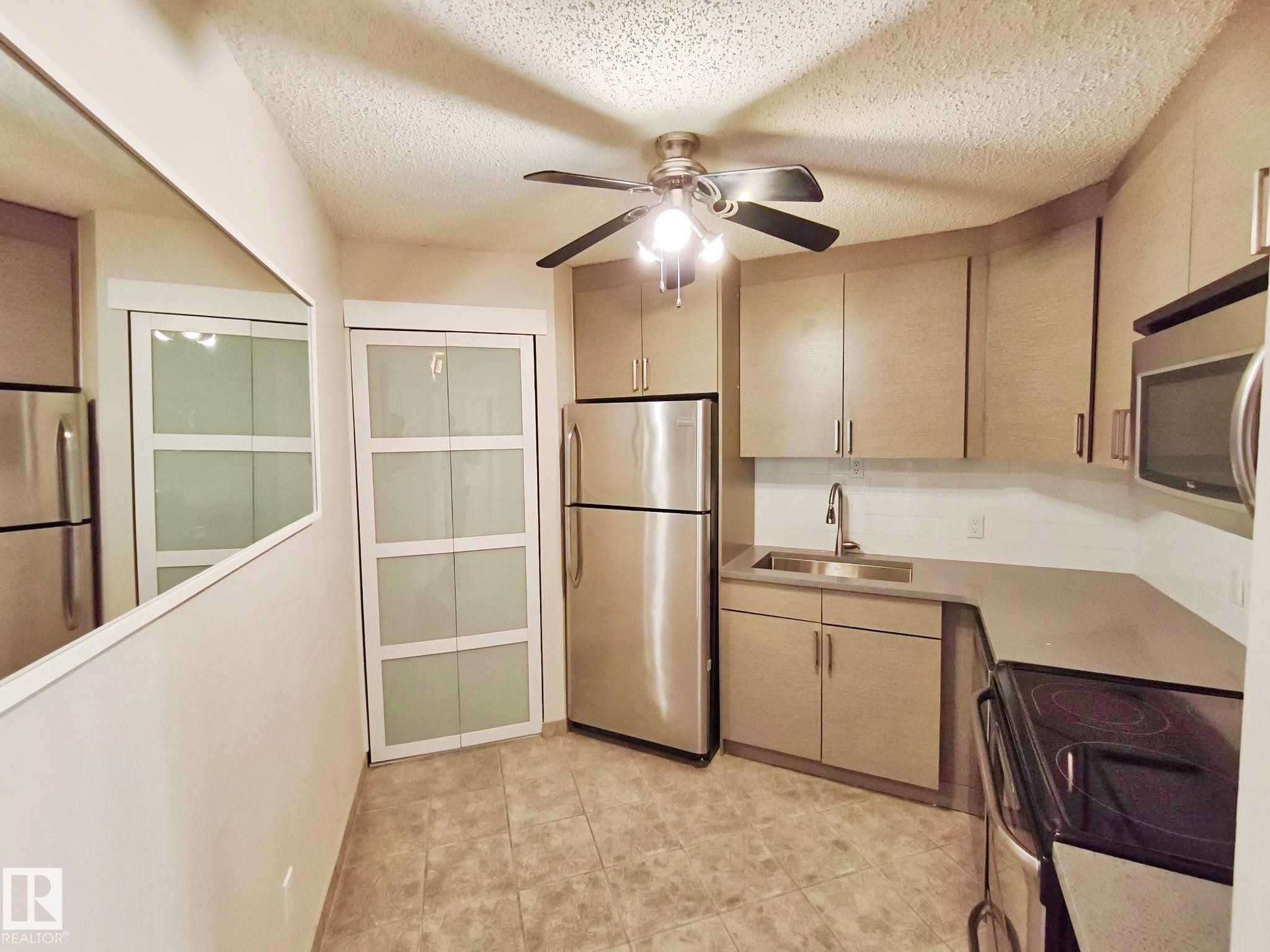 Compact kitchen featuring stainless steel appliances, neutral cabinetry, and light-toned countertops - #509 10149 Saskatchewan Dr Nw, Edmonton, AB - Indoor Photo Showing Kitchen With Stainless Steel Kitchen
