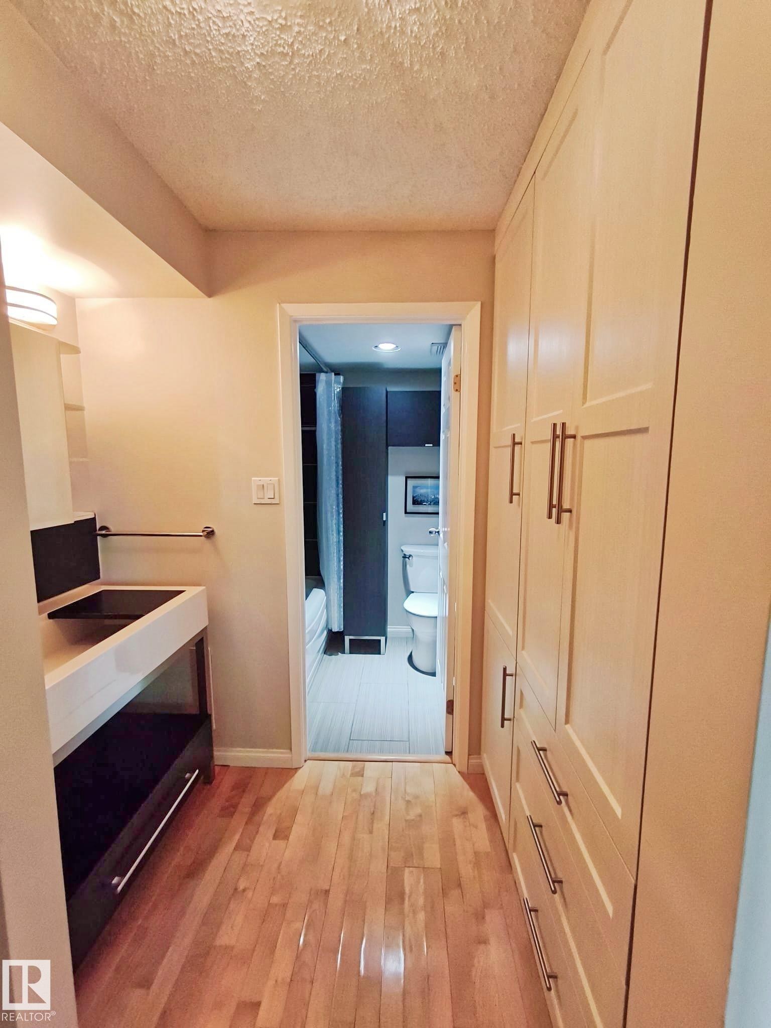 Light wood-finish flooring extending into a bathroom with a white toilet and dark cabinetry - #509 10149 Saskatchewan Dr Nw, Edmonton, AB - Indoor Photo Showing Other Room