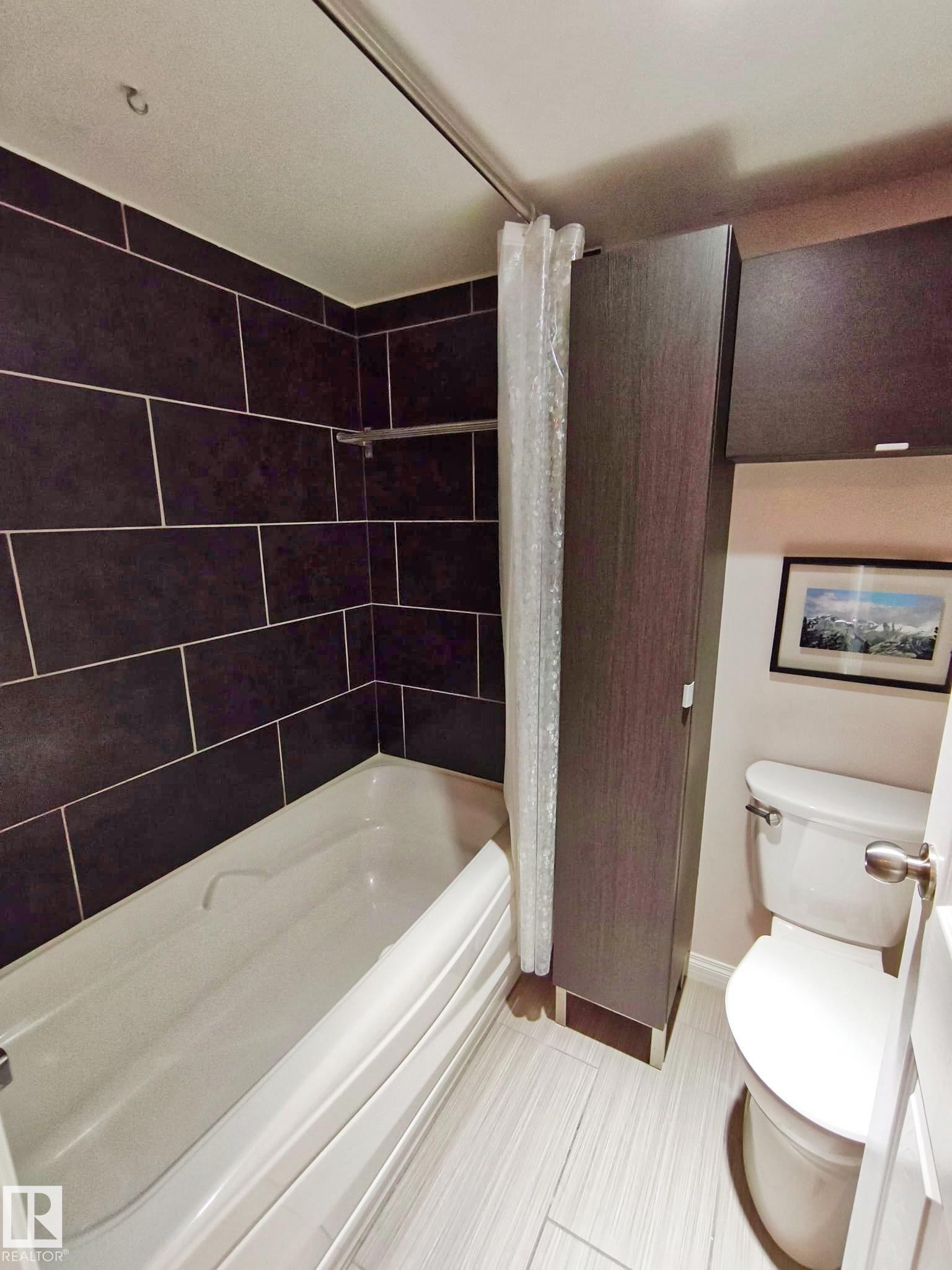 Bathroom featuring a shower/tub combination with dark rectangular wall tiling, white tub, light-toned plank flooring, and a white toilet - #509 10149 Saskatchewan Dr Nw, Edmonton, AB - Indoor Photo Showing Bathroom