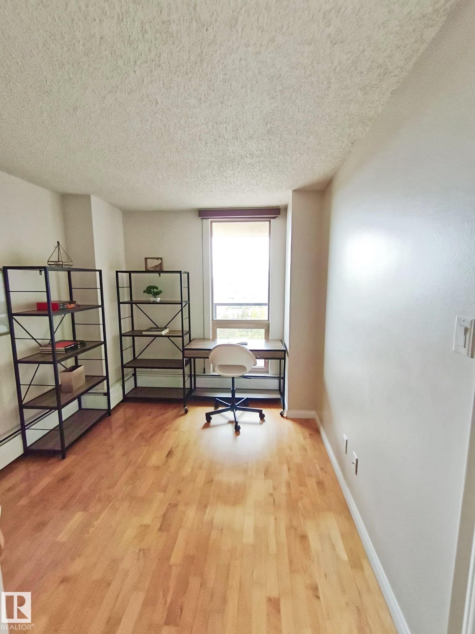 Bright room featuring wood-finish flooring, a window with a roller shade, and white baseboards - #509 10149 Saskatchewan Dr Nw, Edmonton, AB - Indoor