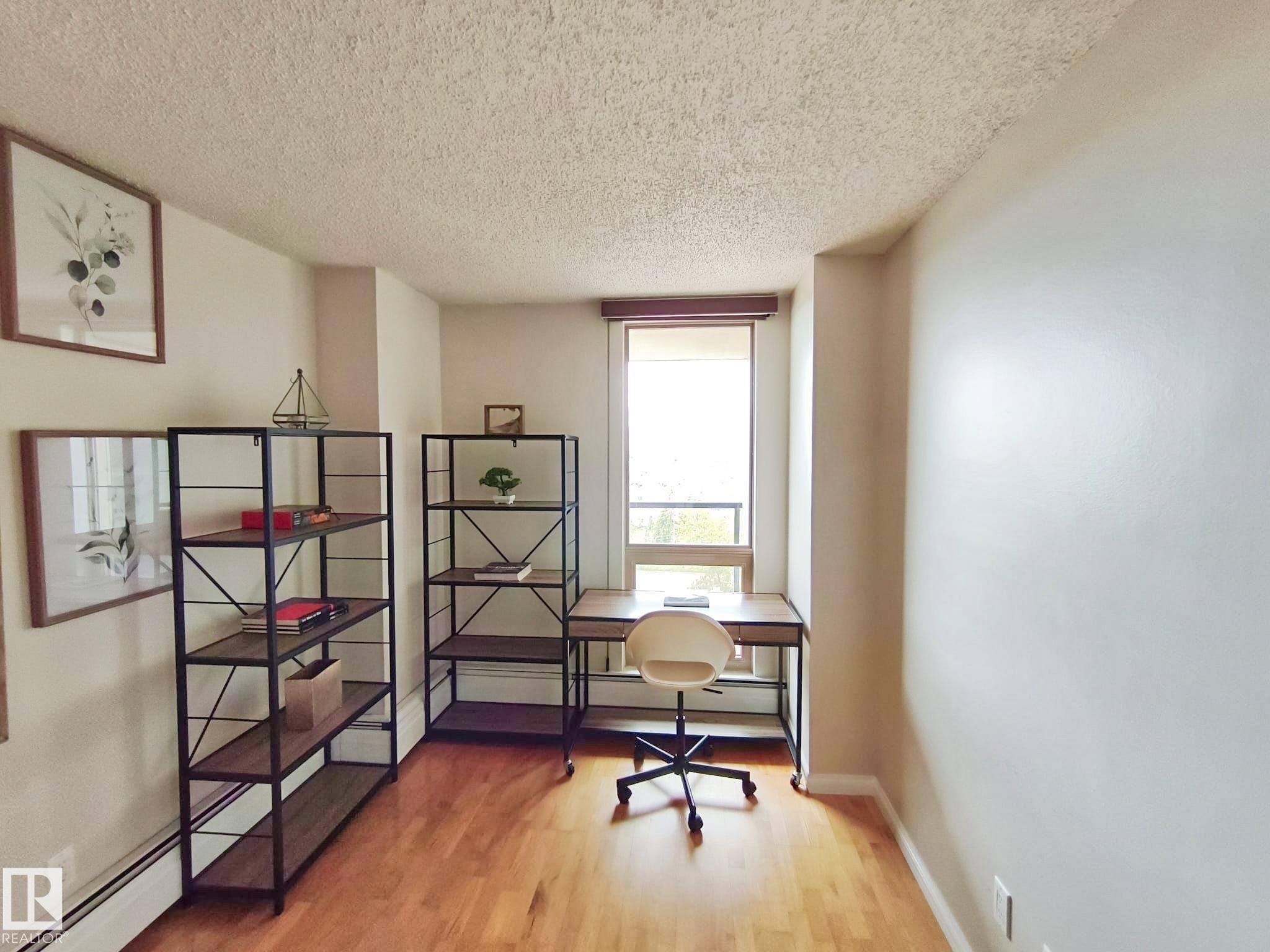 Hardwood-finish flooring highlights this versatile room, featuring a large window with natural light, baseboard heating, and smooth wall finishes - #509 10149 Saskatchewan Dr Nw, Edmonton, AB - Indoor Photo Showing Office
