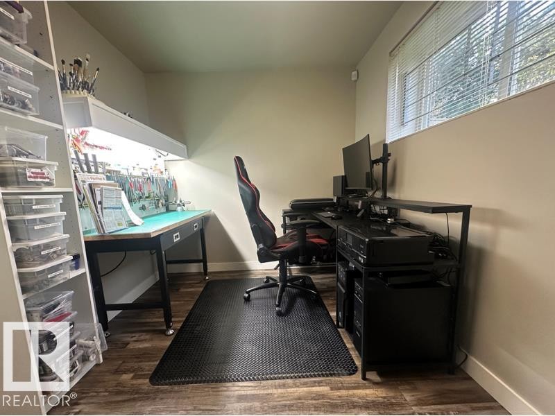Dedicated workspace featuring wood-finish flooring, a built-in shelving unit, and a window with horizontal blinds - 10416 148 Street Nw, Edmonton, AB - Indoor Photo Showing Office