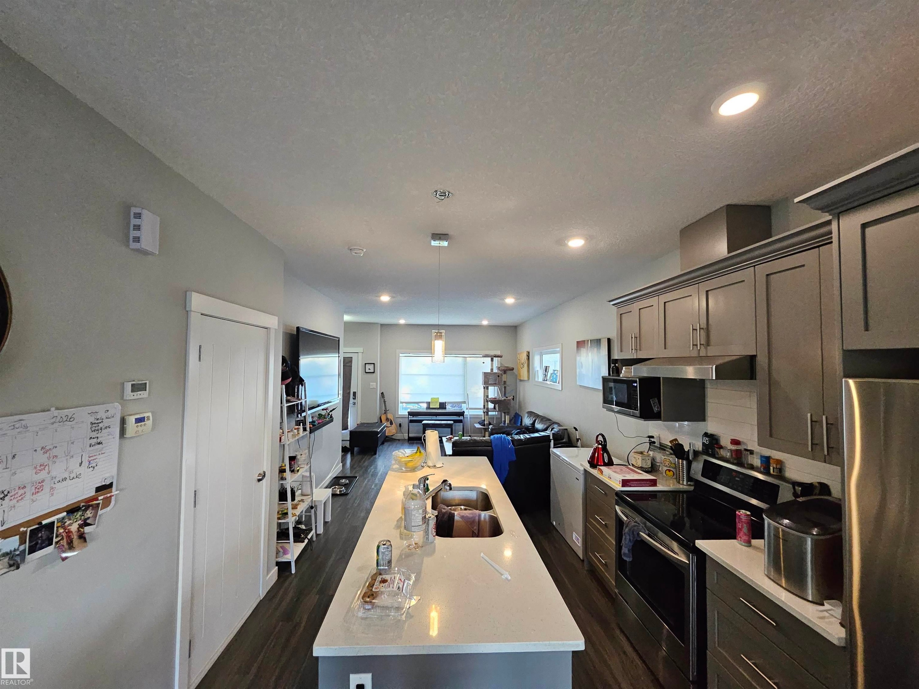 Open concept kitchen featuring an extended island with a double sink, gray cabinetry, stainless steel appliances, and wood-finish flooring - 13309 104 Street Nw, Edmonton, AB - Indoor Photo Showing Kitchen With Upgraded Kitchen