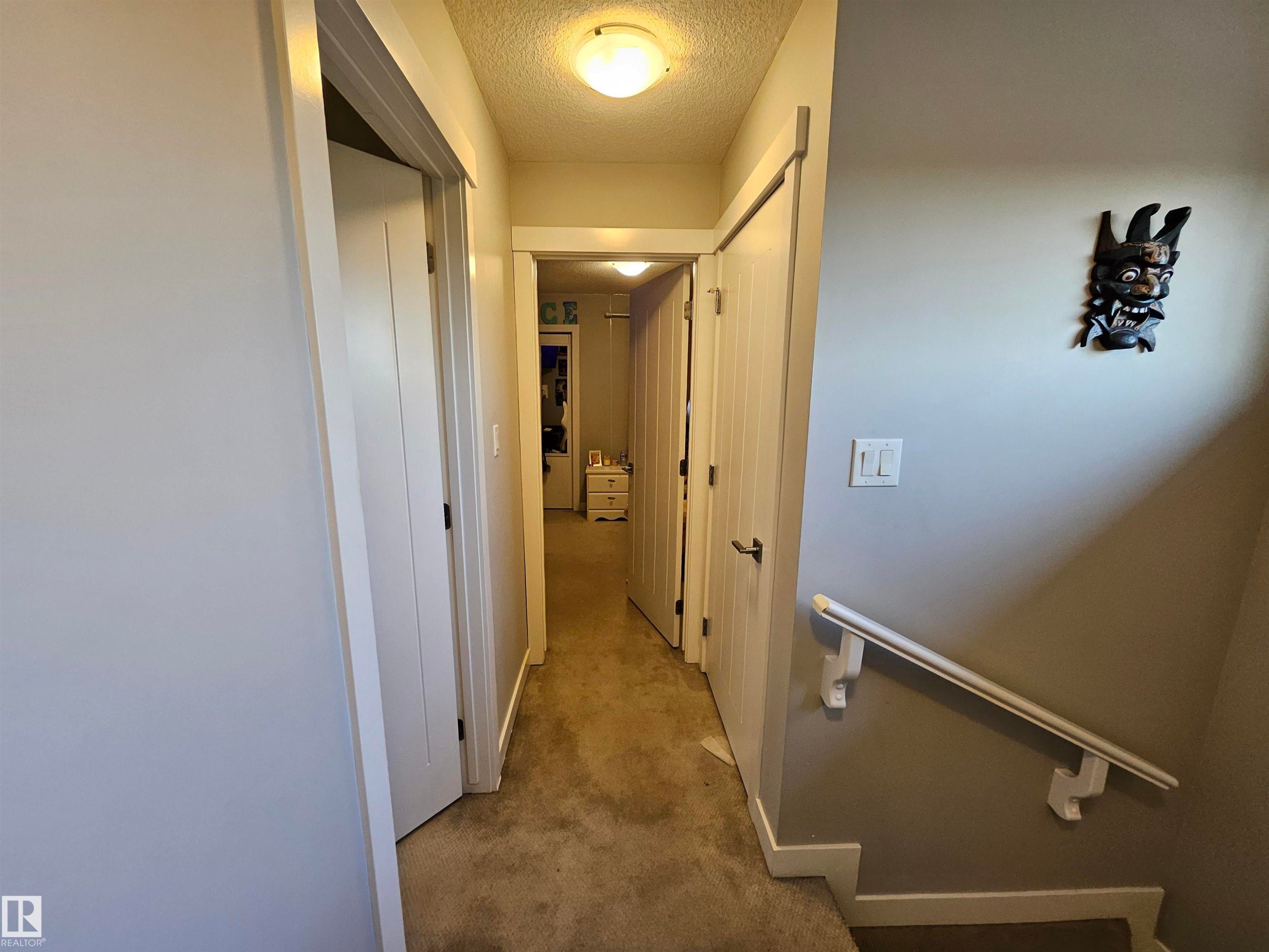 Carpeted hallway featuring white trim and doors, flush-mount lighting, and a wall-mounted handrail - 13309 104 Street Nw, Edmonton, AB - Indoor Photo Showing Other Room