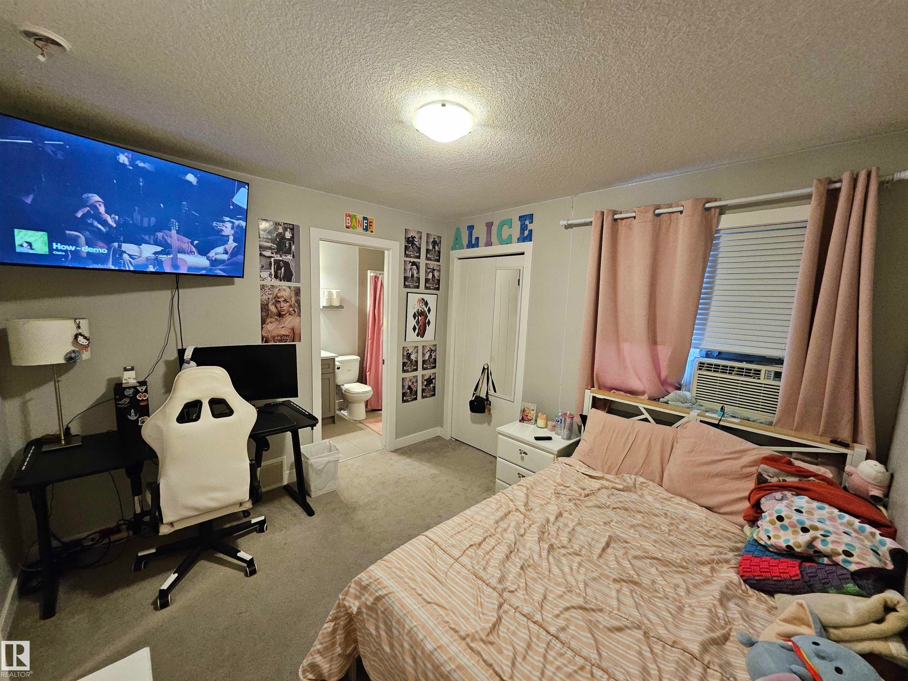 Carpeted room featuring a ceiling-mounted light fixture, an integrated wall air conditioning unit, and a doorway leading to an additional space - 13309 104 Street Nw, Edmonton, AB - Indoor Photo Showing Bedroom