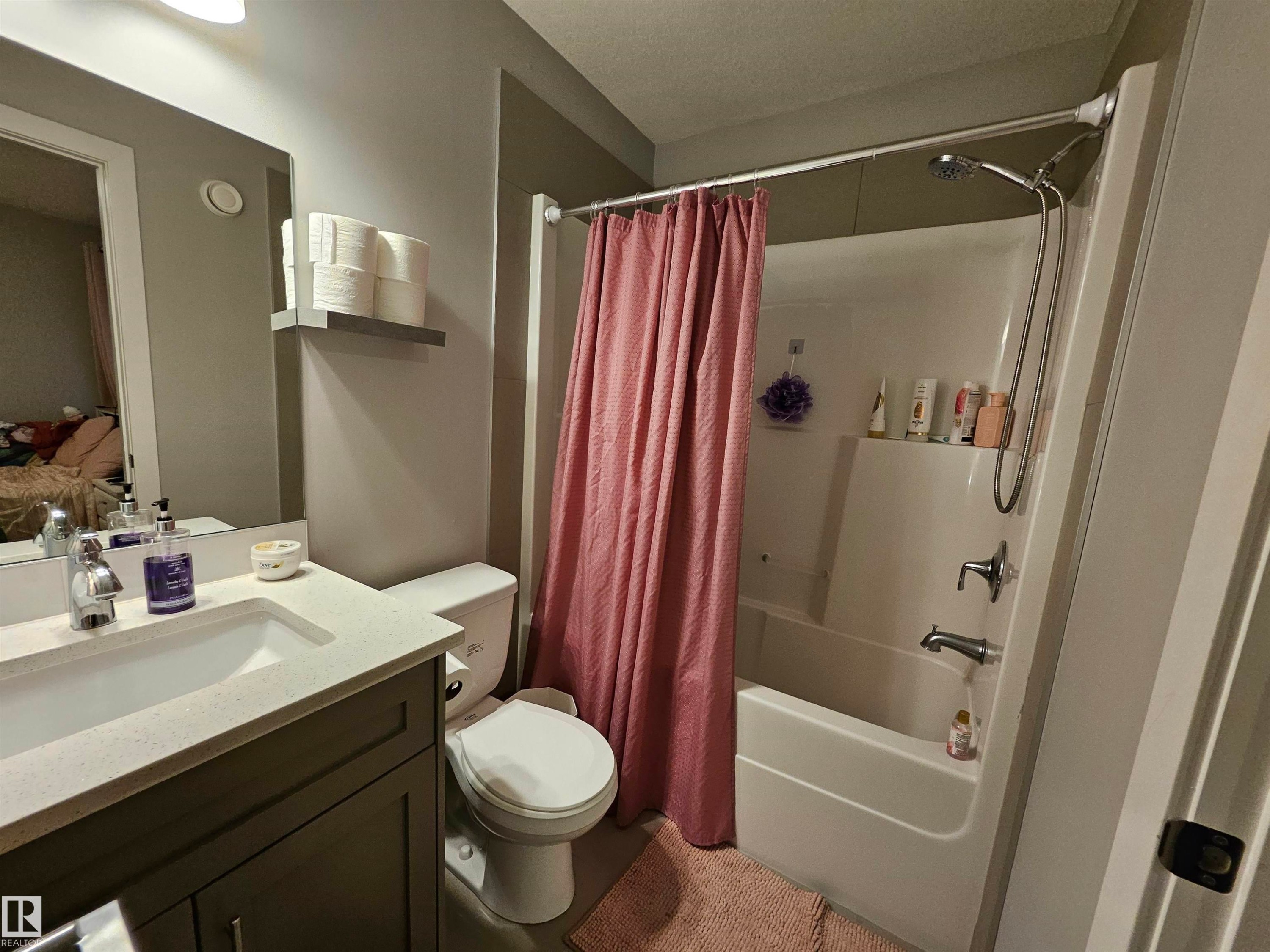 Bathroom featuring a vanity with a light-colored countertop and integrated sink, a white toilet, and a white tub with an overhead shower fixture - 13309 104 Street Nw, Edmonton, AB - Indoor Photo Showing Bathroom