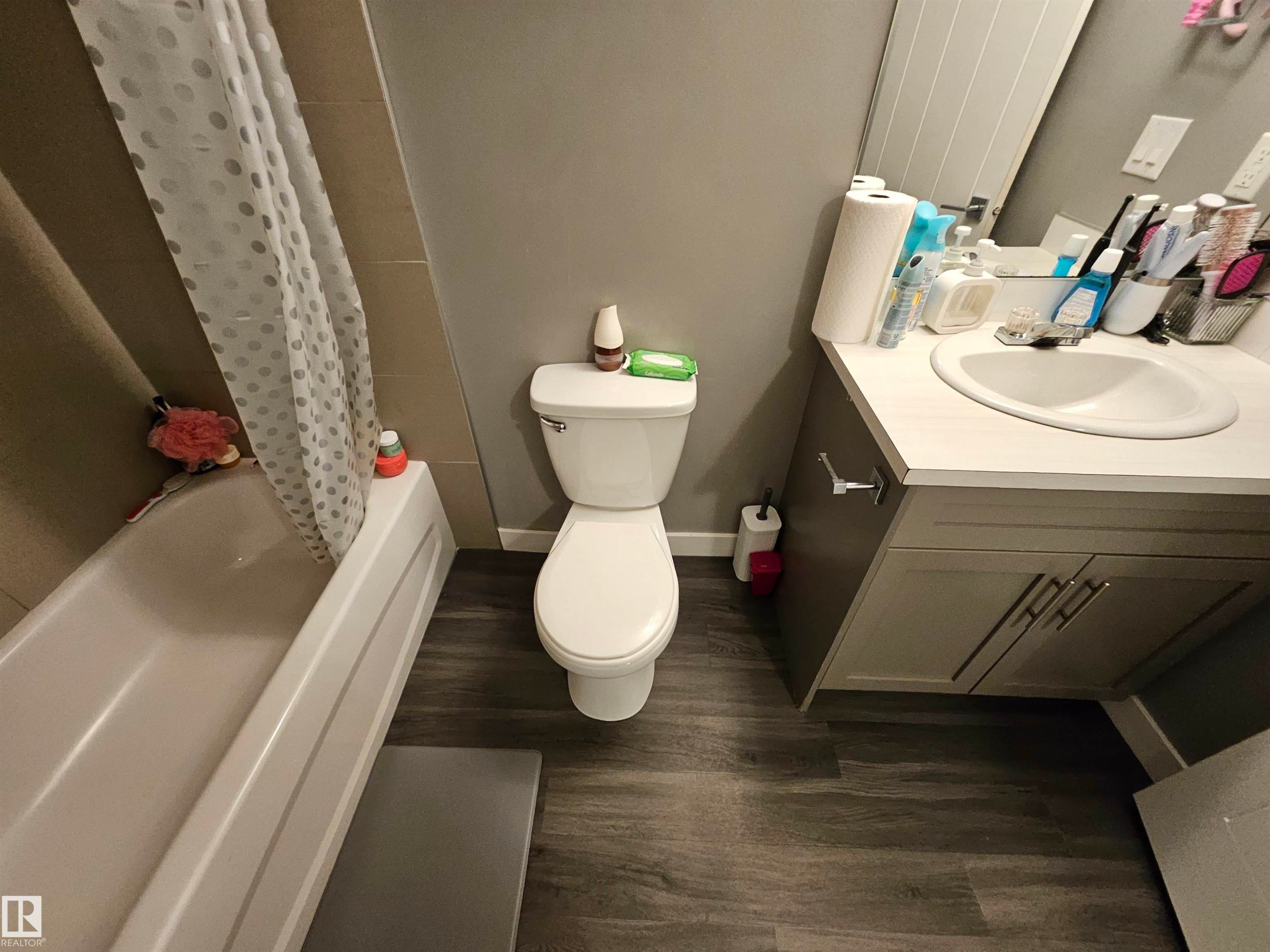 Bathroom featuring wood-finish flooring, a white bathtub, a toilet, and a vanity with an integrated sink and base cabinetry - 13309 104 Street Nw, Edmonton, AB - Indoor Photo Showing Bathroom
