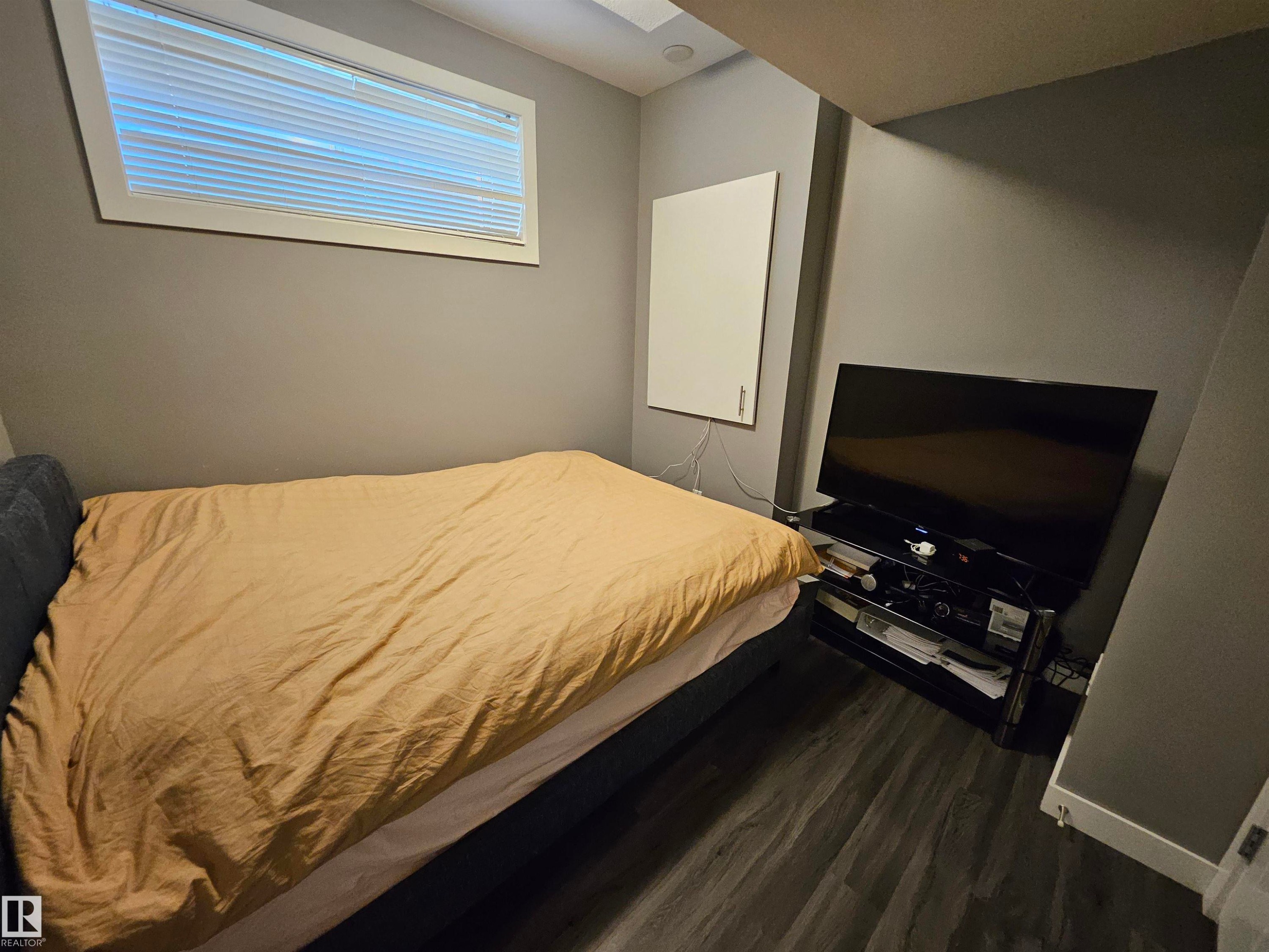 Room featuring wood-finish flooring, a rectangular window with blinds, and neutral gray walls - 13309 104 Street Nw, Edmonton, AB - Indoor Photo Showing Bedroom