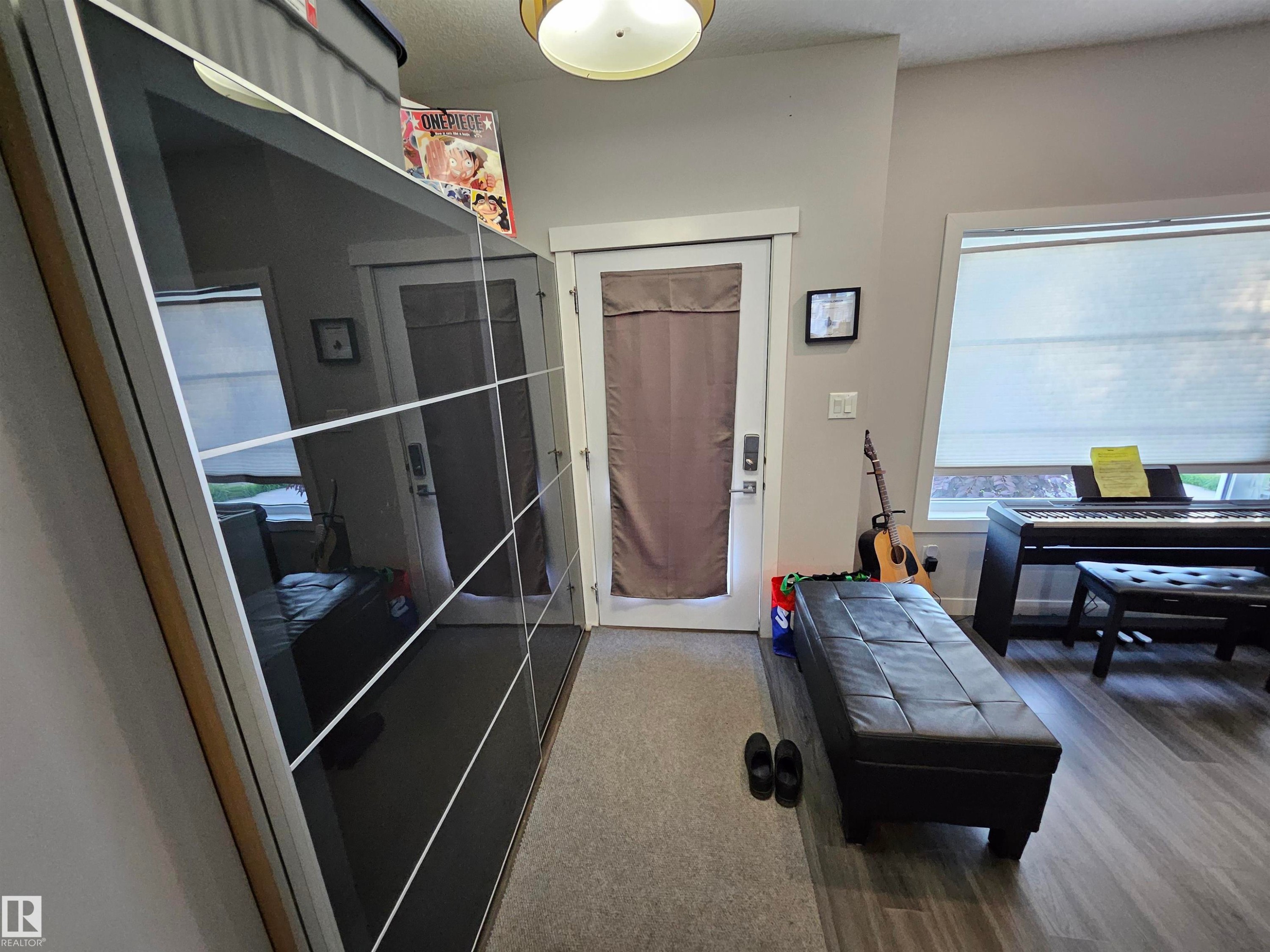 Modern hallway featuring wood-finish flooring, a white trim window with blinds, and a built-in closet with reflective paneled doors - 13309 104 Street Nw, Edmonton, AB - Indoor Photo Showing Other Room