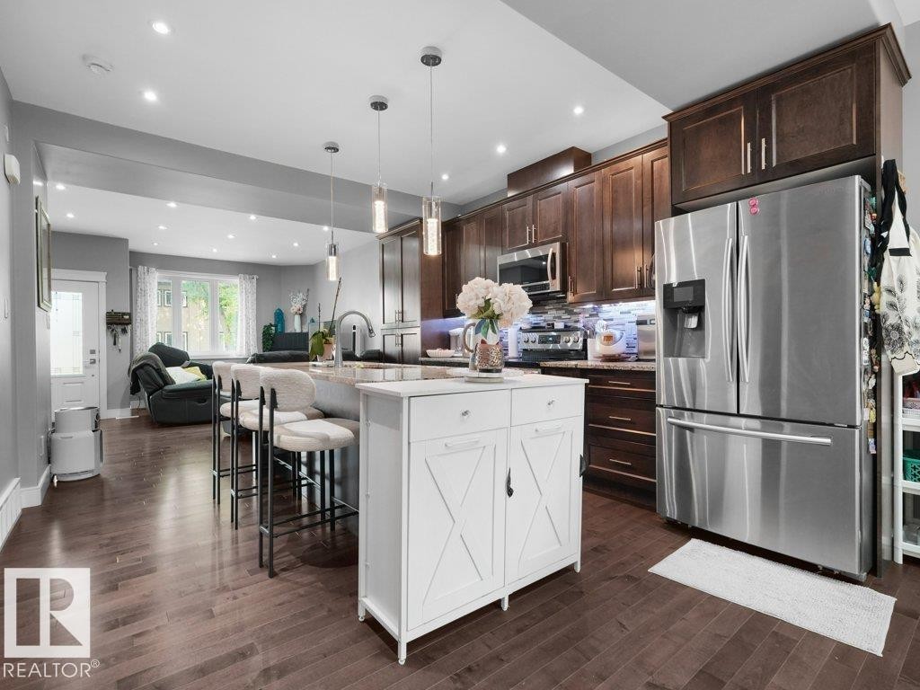 Open-concept kitchen featuring dark wood-finish flooring, recessed lighting, a kitchen island with pendant lights, dark wood cabinetry, and stainless steel appliances - 7909 105 Avenue Nw, Edmonton, AB - Indoor Photo Showing Kitchen With Upgraded Kitchen