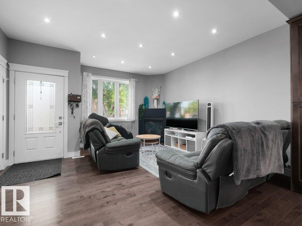 Living area featuring wood-finish flooring, recessed lighting, a white framed window with decorative curtains, and a white entry door with frosted glass panels - 7909 105 Avenue Nw, Edmonton, AB - Indoor