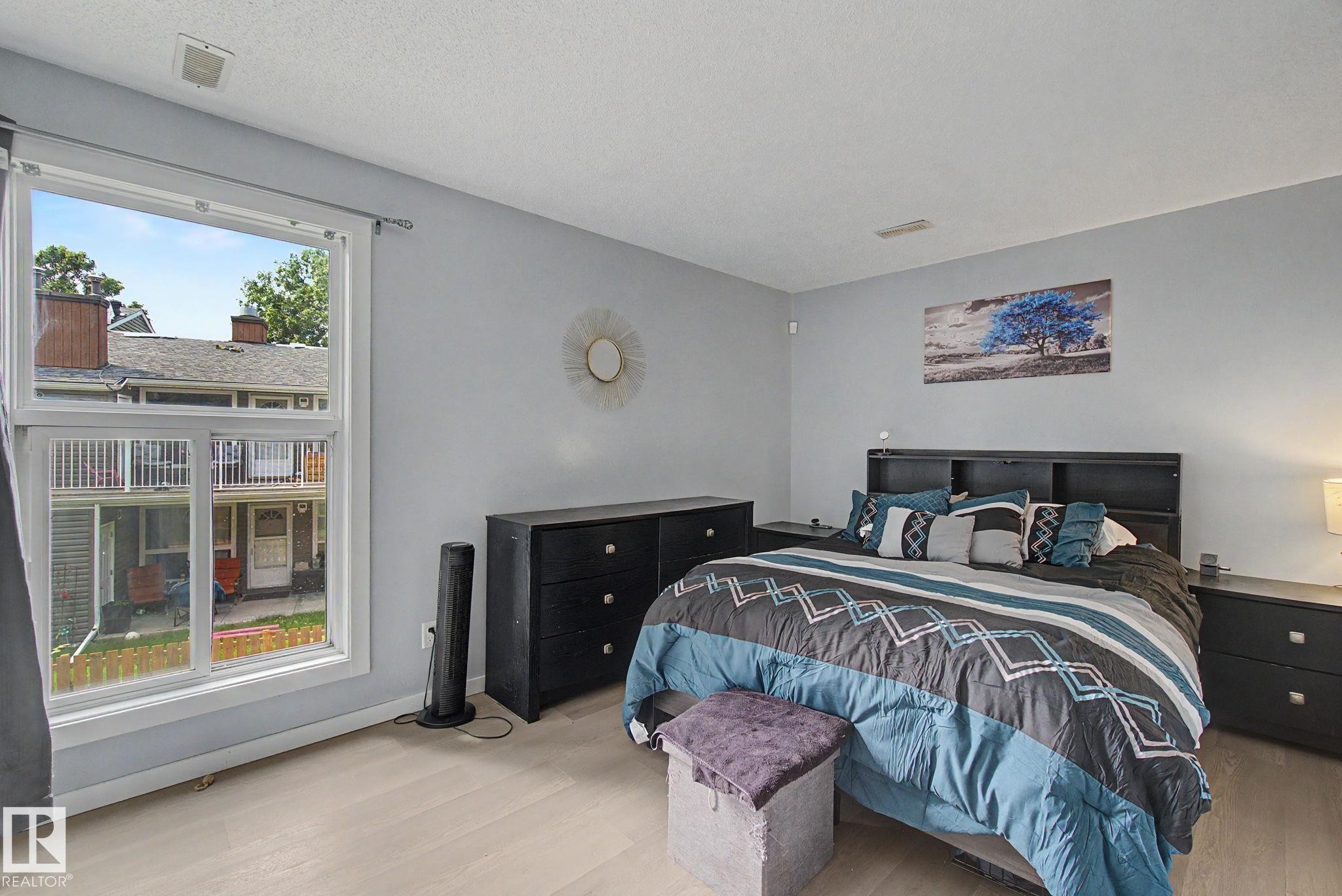 Bright interior space featuring light-toned wood-finish flooring, a large window, and light gray walls - #39 3111 142 Av Nw, Edmonton, AB - Indoor Photo Showing Bedroom