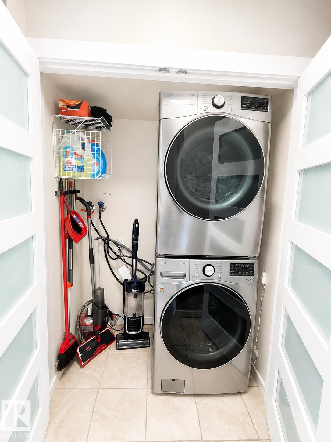Dedicated laundry closet featuring a stackable washer and dryer, tile flooring, and frosted glass bi-fold doors - #39 3111 142 Av Nw, Edmonton, AB - Indoor Photo Showing Laundry Room