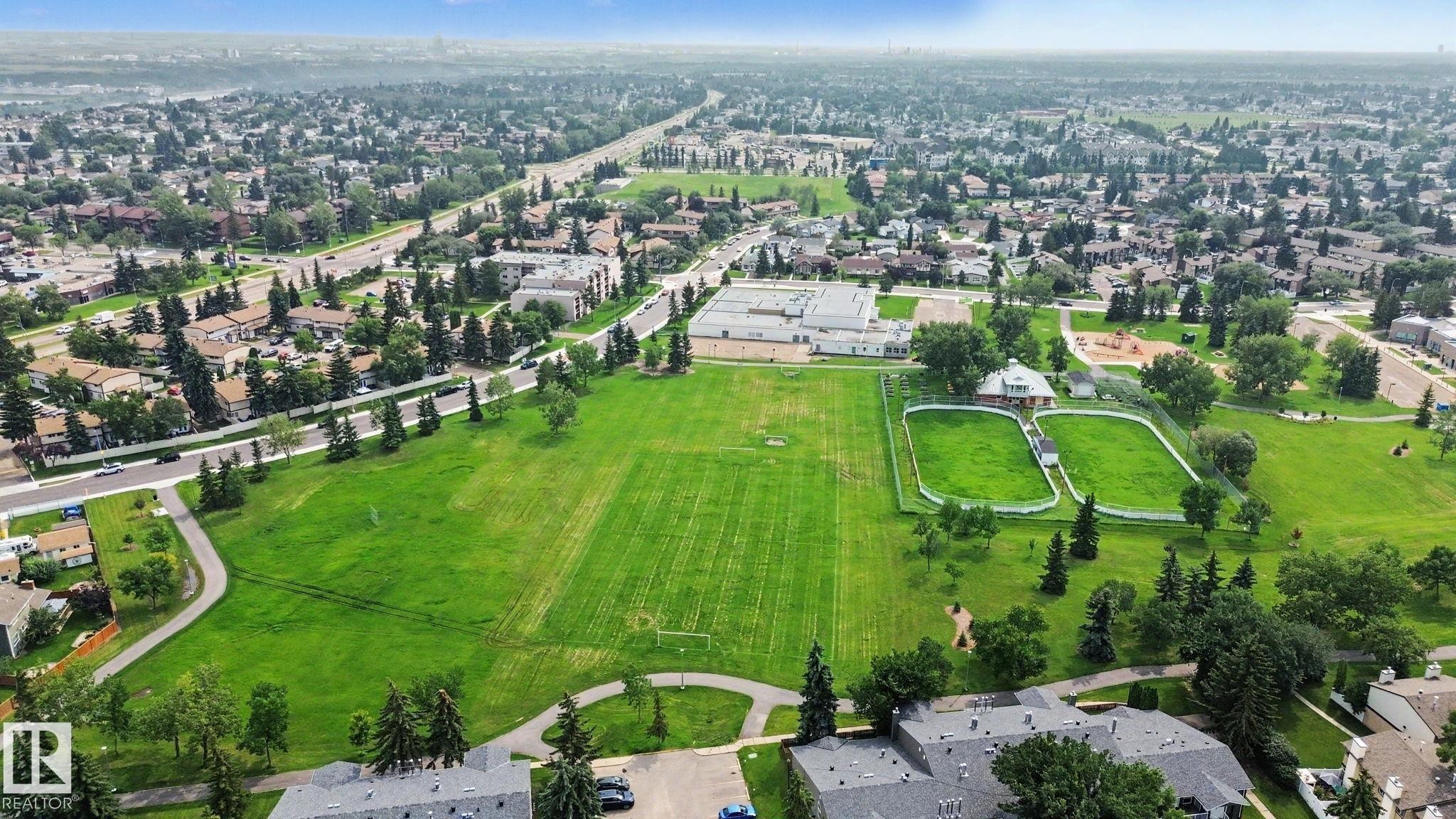 Expansive green spaces featuring a large sports field, walking paths, and two enclosed recreational areas - #39 3111 142 Av Nw, Edmonton, AB - Outdoor With View